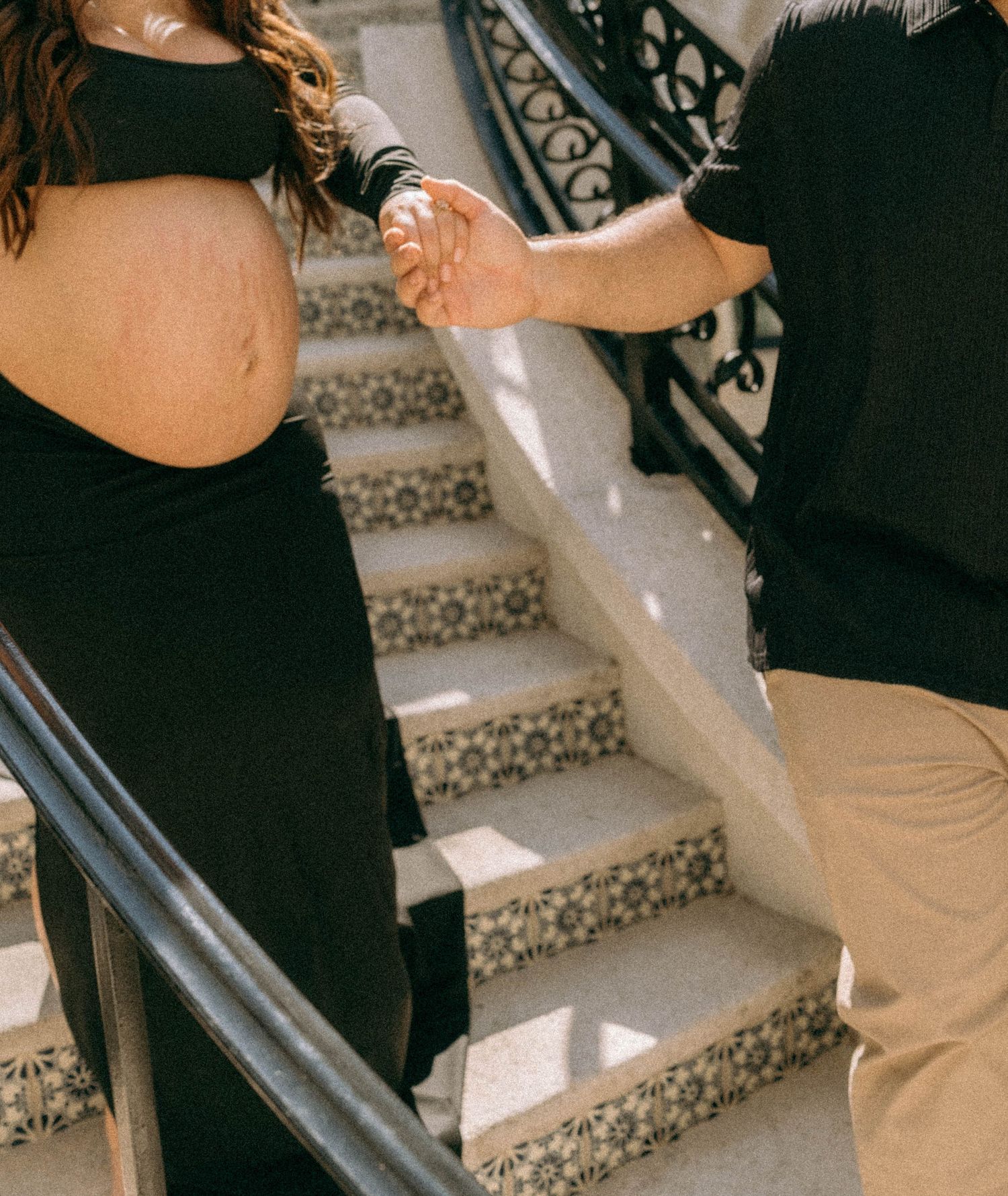 Pregnant woman in black dress holding hands with partner on decorative tiled steps outdoors. Worth Avenue, Palm Beach, FL