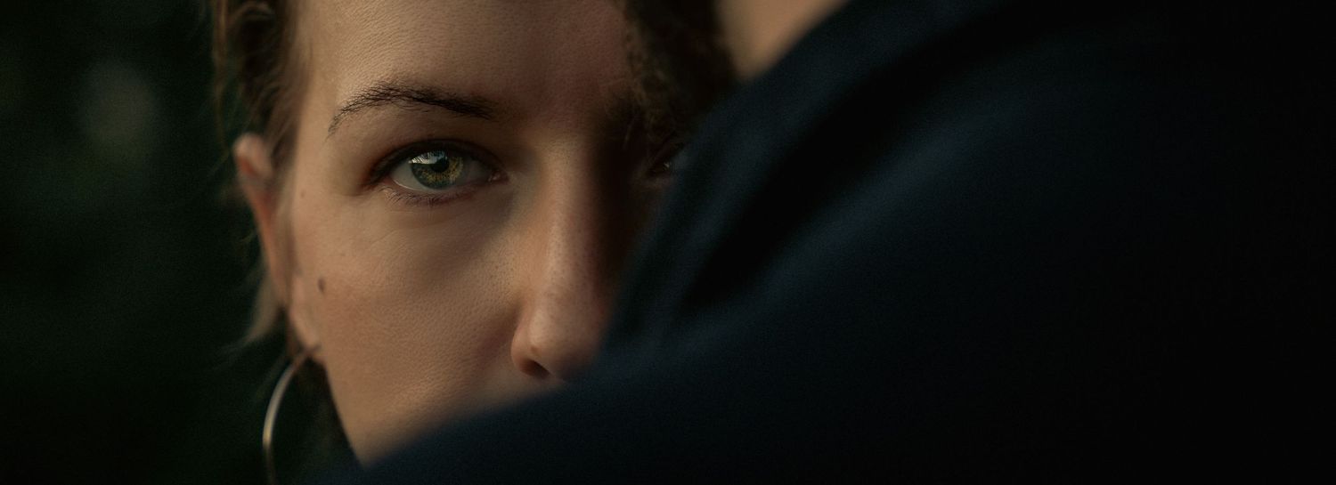 Close-up of a woman with blue eyes and dark hair, gazing intensely in a dramatic, moody cinematic scene.