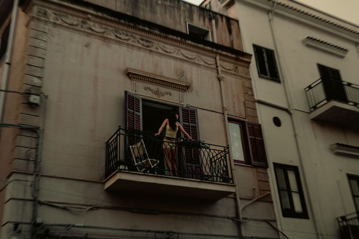 Person standing on ornate balcony of aged European building with weathered facade and decorative architectural details.