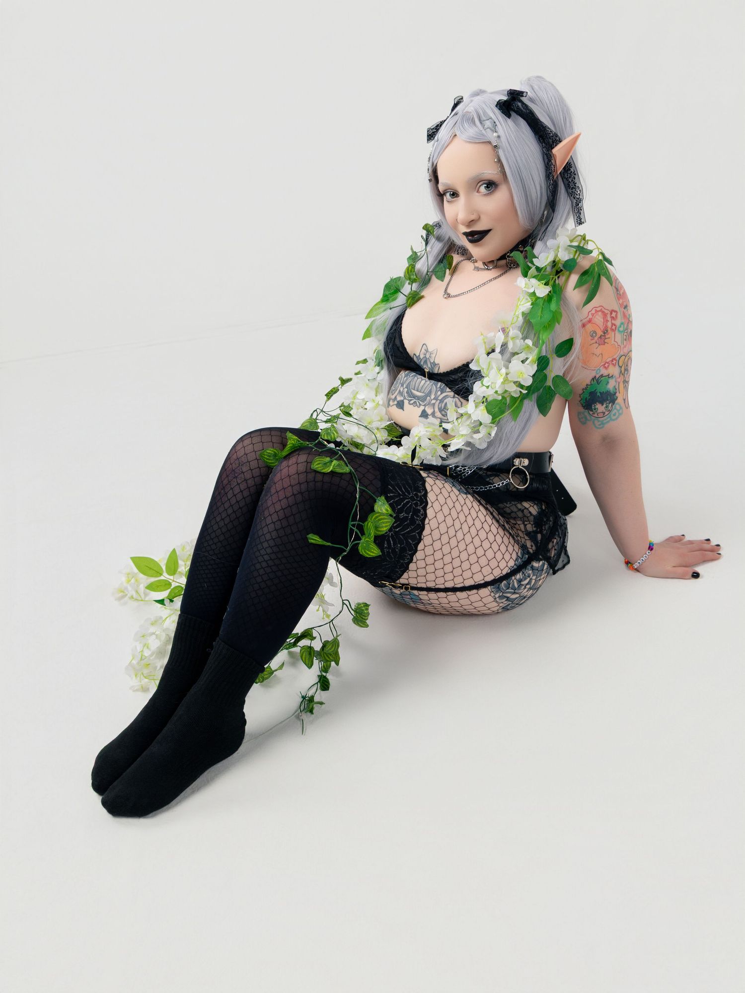 Model in black fishnet and white flowers poses artistically on light background.