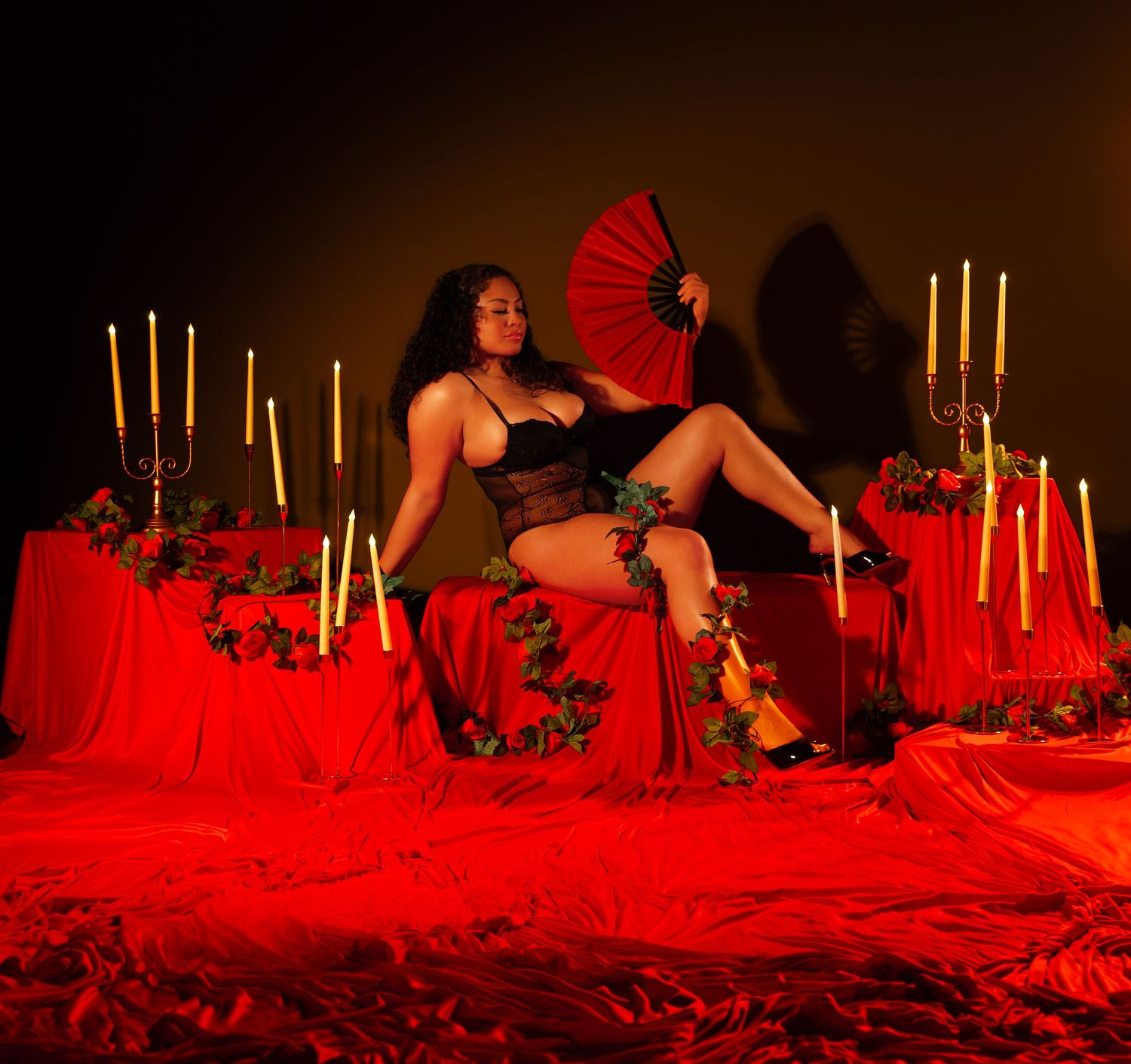 Artistic boudoir photoshoot setup with red lighting, white candles, and dark ambiance creating a romantic atmosphere.