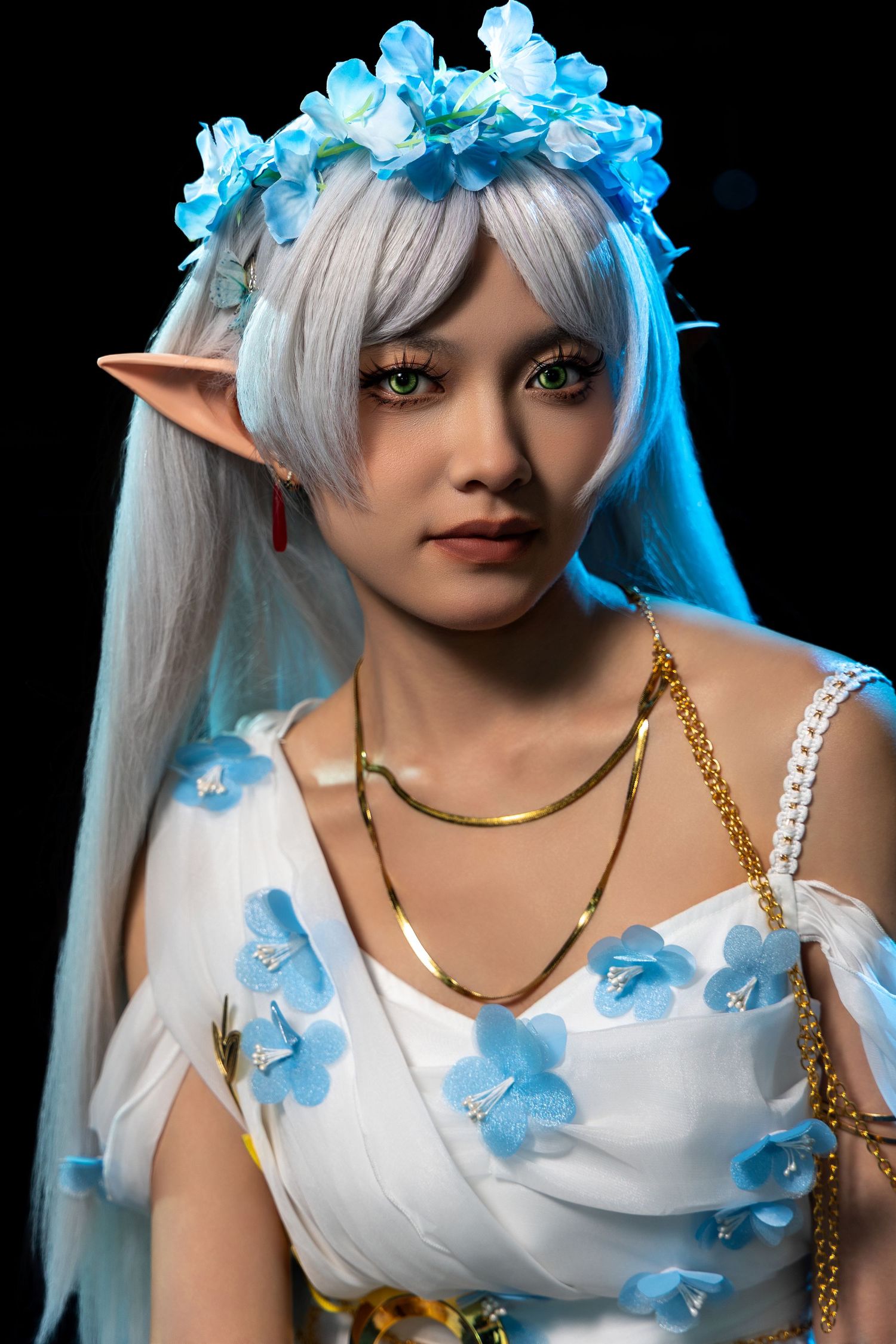 Fantasy cosplay featuring ethereal elf character with blue flower crown and white floral dress.