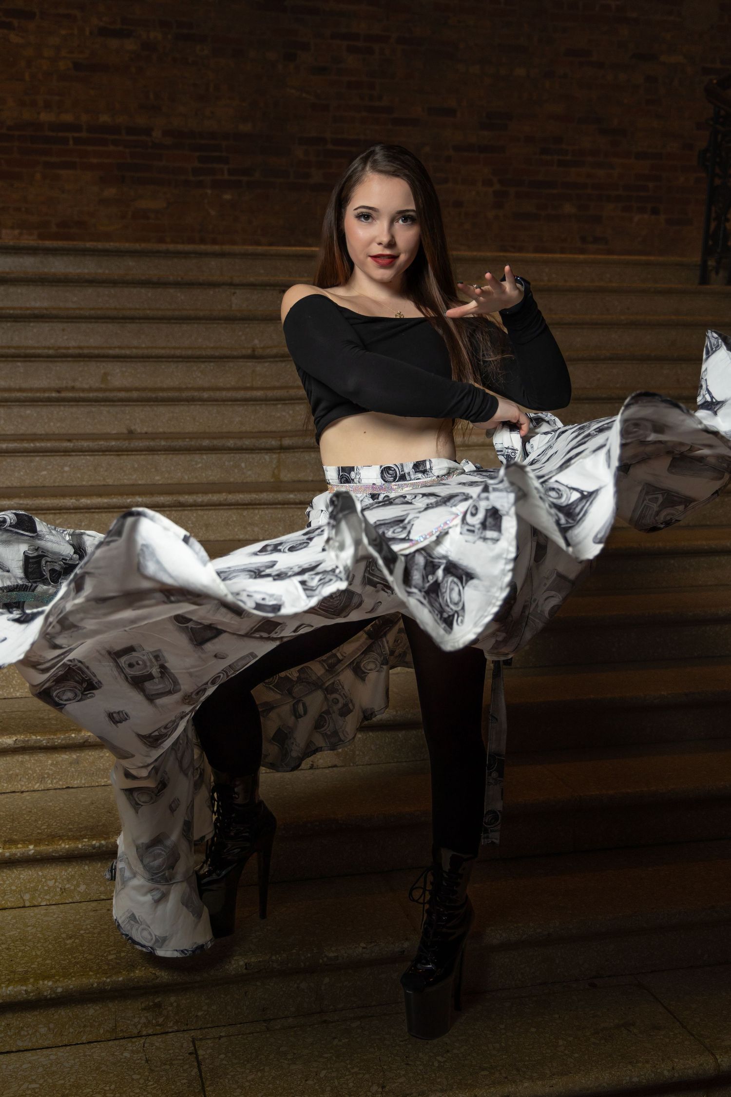 Dancer in black crop top with flowing newspaper-print fabric in dramatic lighting.