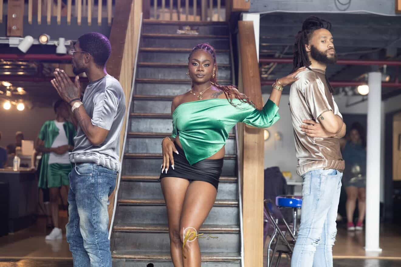 Three people strike confident poses on stairs in a nightclub setting, wearing stylish casual outfits including green and metallic tops.