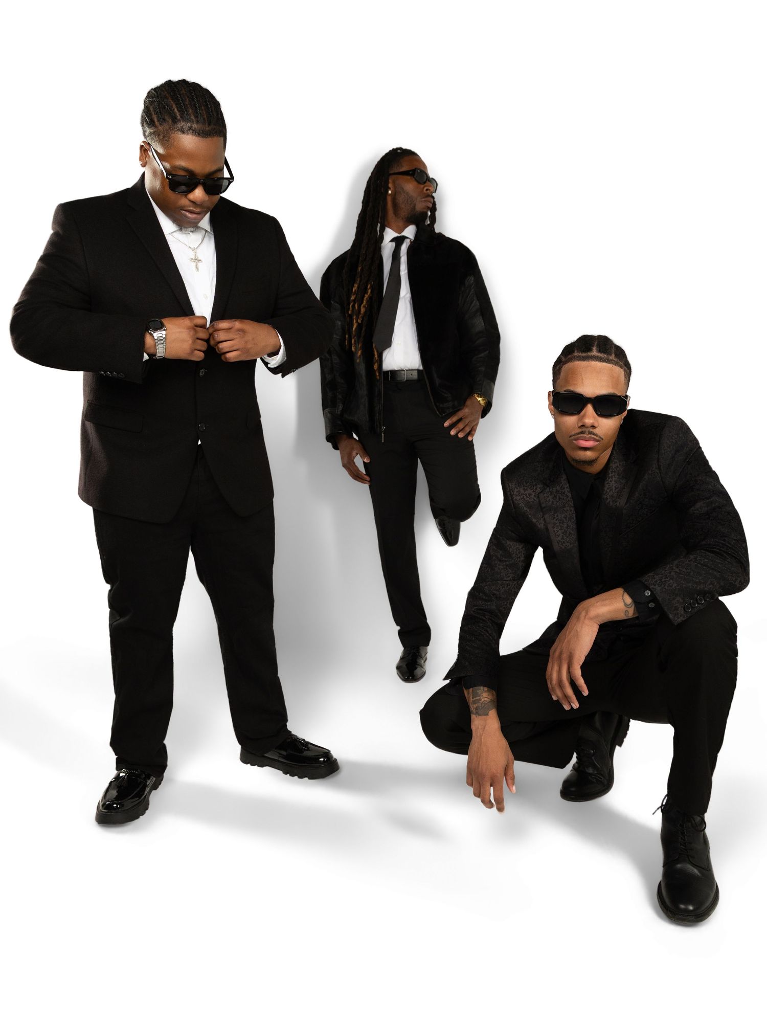 Professional group photo of three people in black suits and sunglasses against white background.