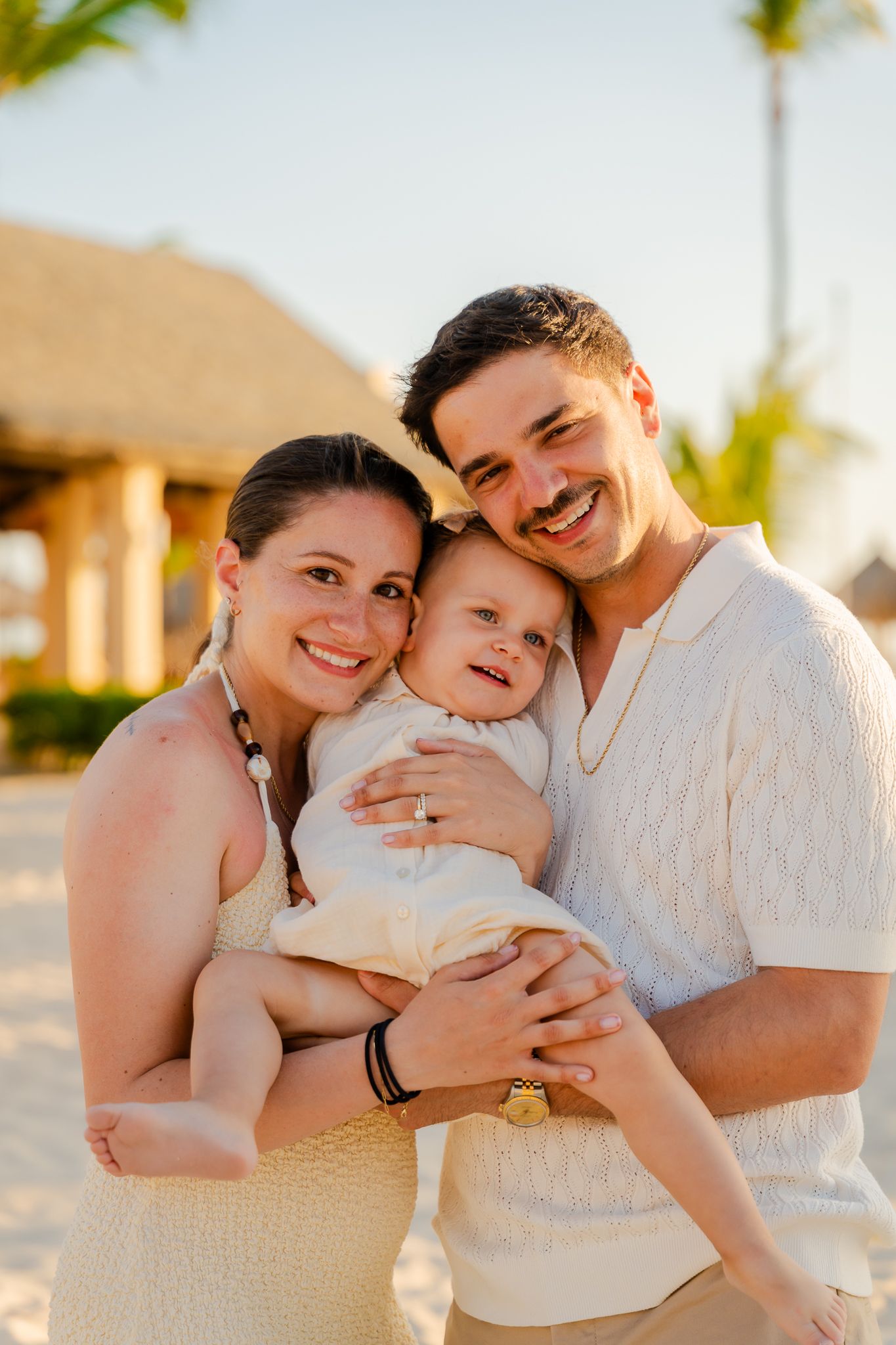Happy young family with baby smiling together on a sunny beach resort at golden hour.