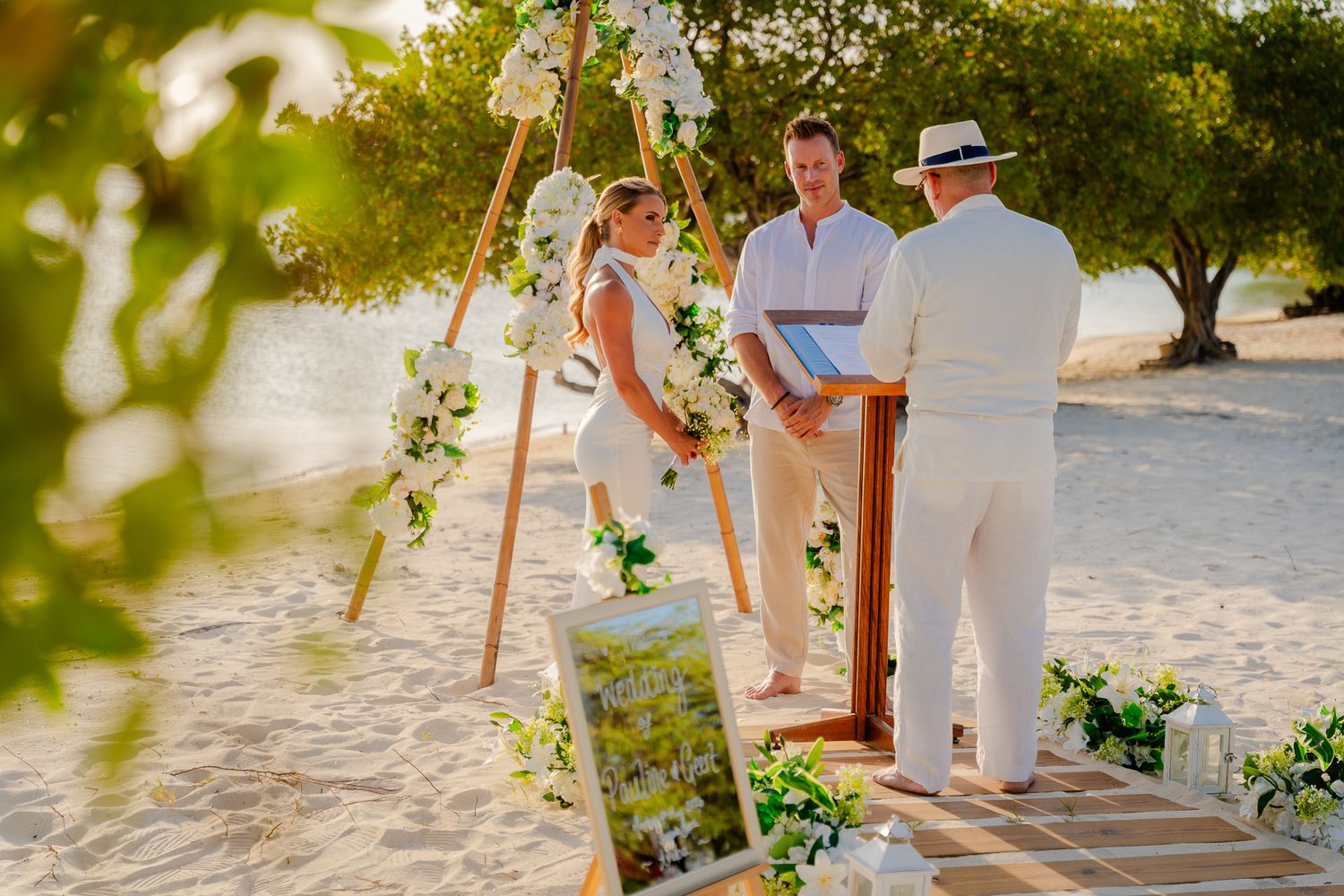Couple exchanging vows at a romantic beach wedding ceremony with white floral arch and officiant.