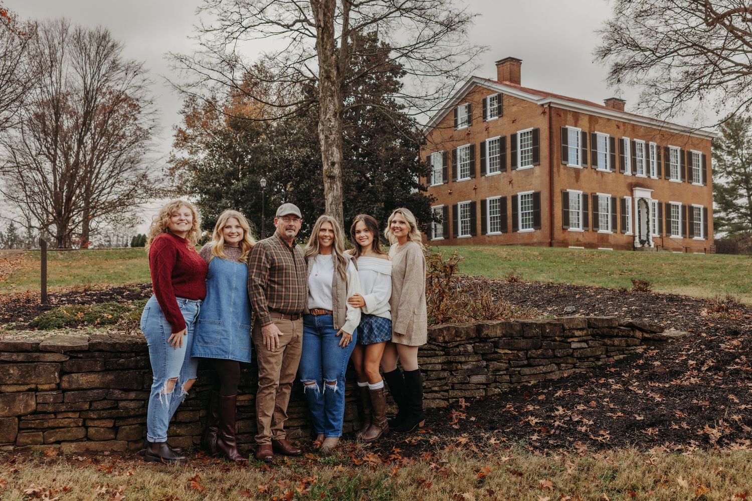 Large family gathering posed along stone wall with brick mansion in background.