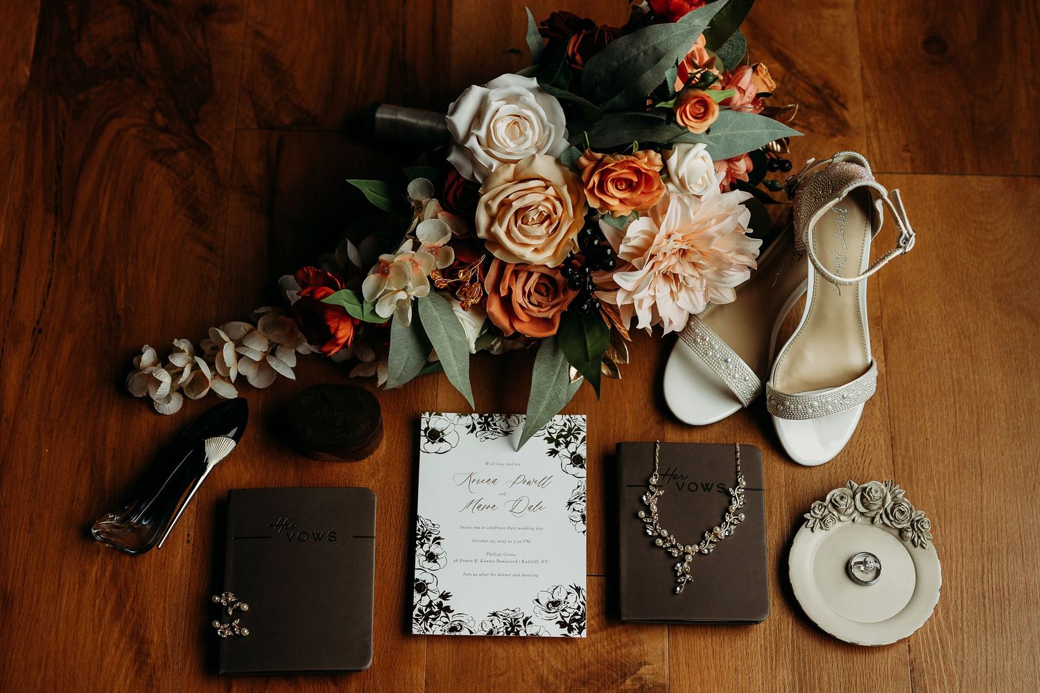 Wedding flat lay with floral bouquet, white heels, invitations, jewelry, and accessories on wooden surface.