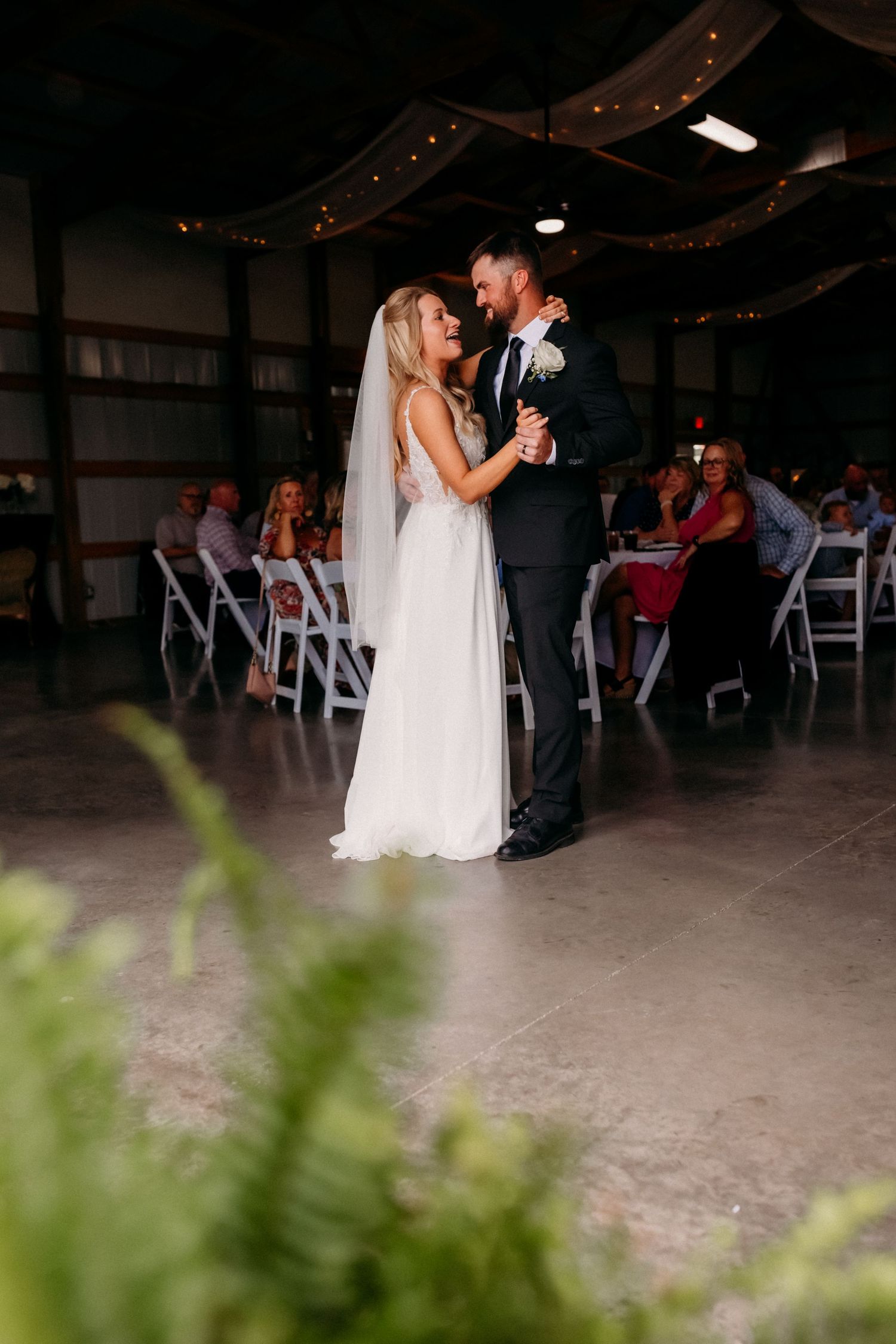 Bride and groom share first dance in rustic barn venue surrounded by wedding guests.
