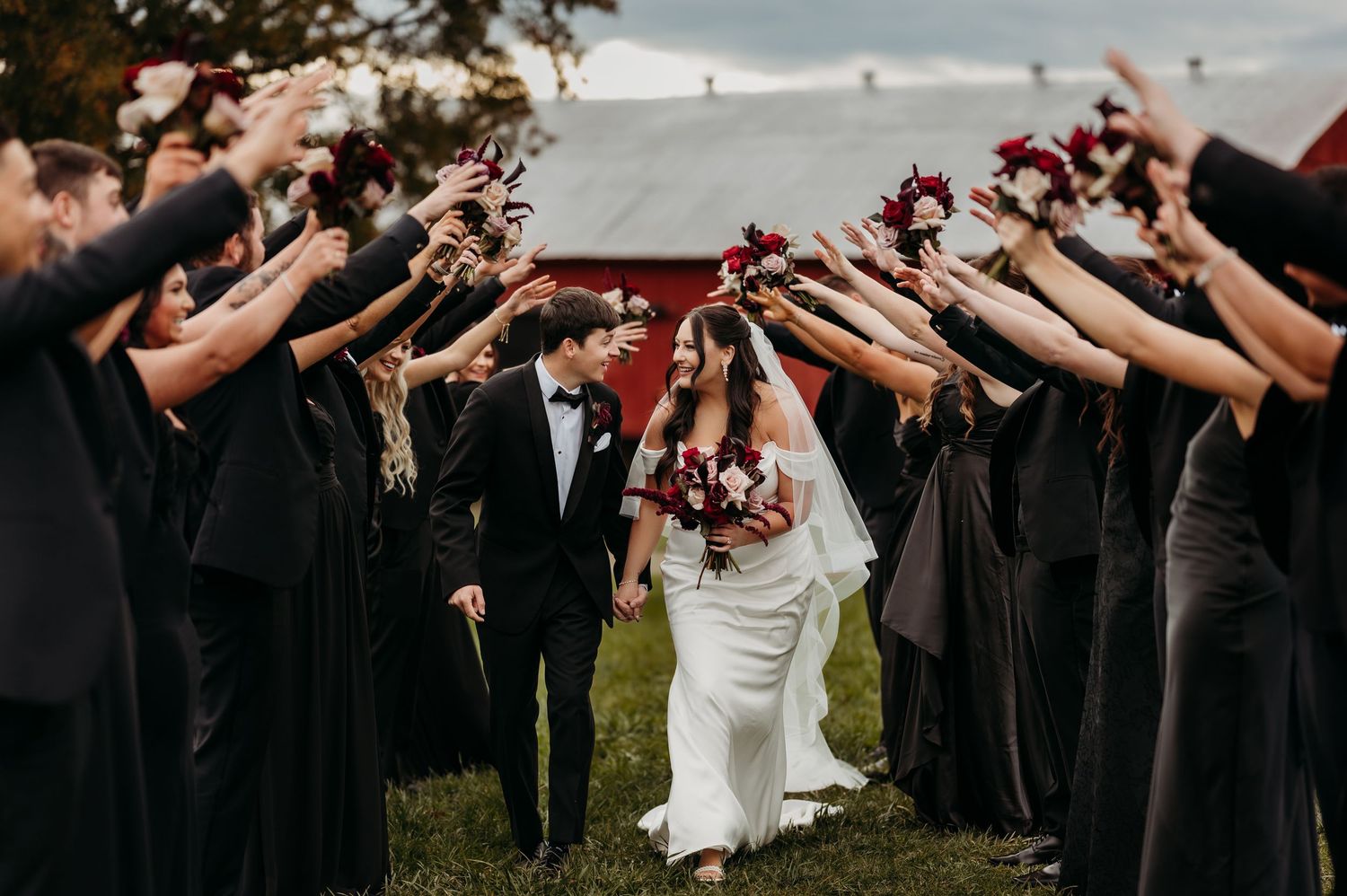 The wedding party forms an aisle while holding bouquets in the air as the newlyweds walk through.