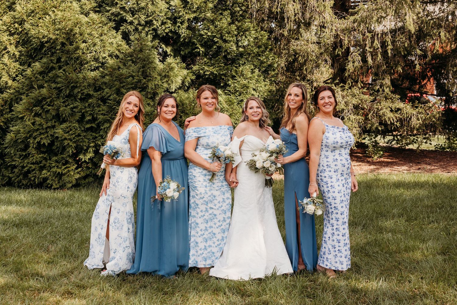 Wedding party members in blue and white dresses posing together outdoors.