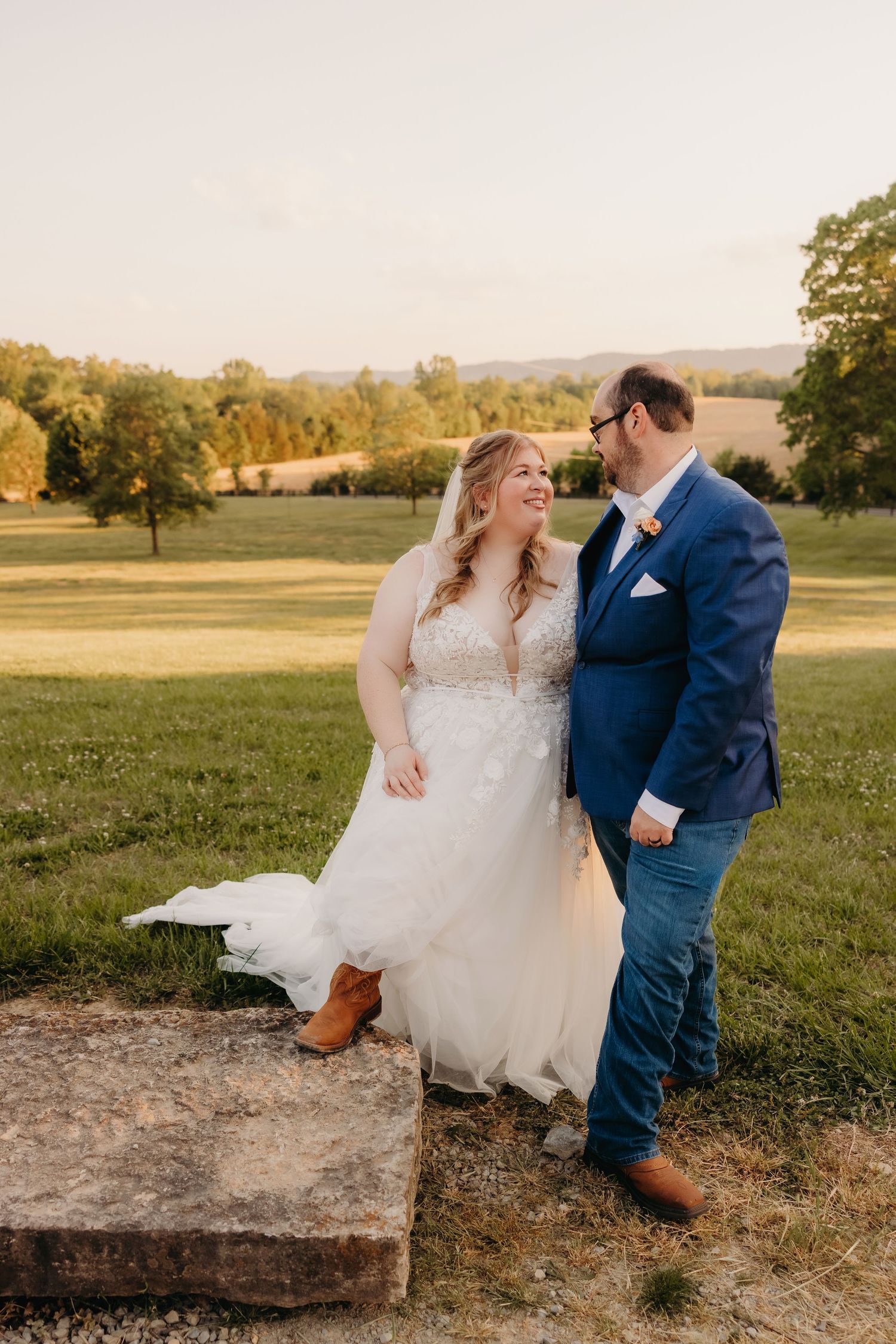 Bride and groom sharing joyful moment at golden hour in scenic green countryside setting.
