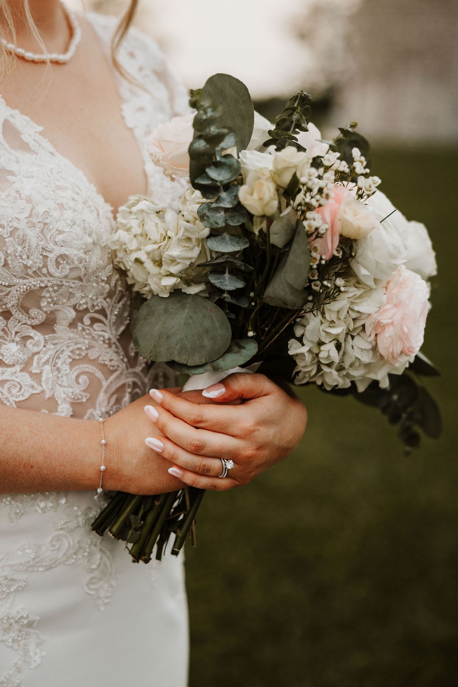 Close-up detail of a wedding bouquet with white flowers and greenery against a lace dress.