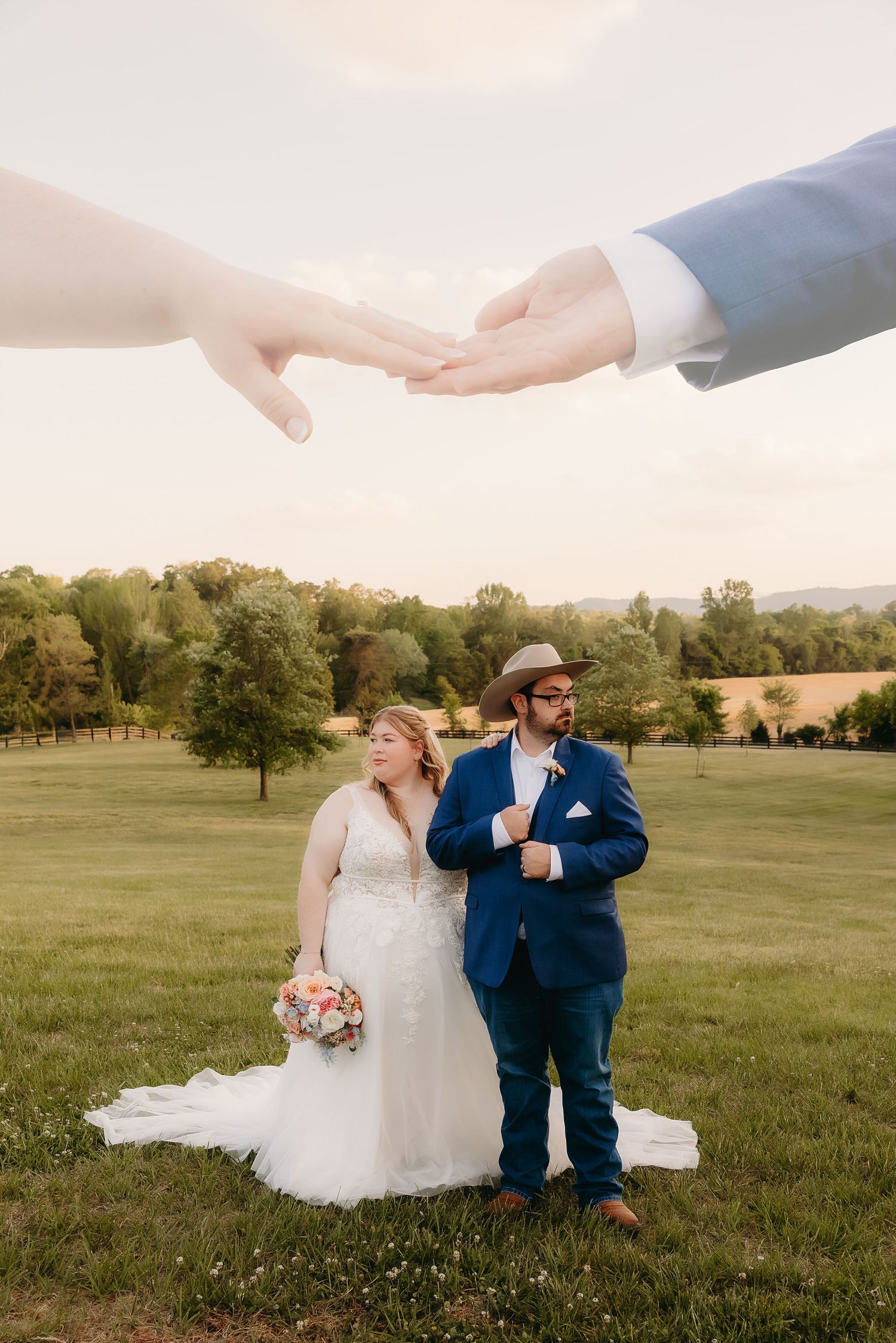 Bride and groom pose outdoors as large hands frame them from above in creative wedding portrait.