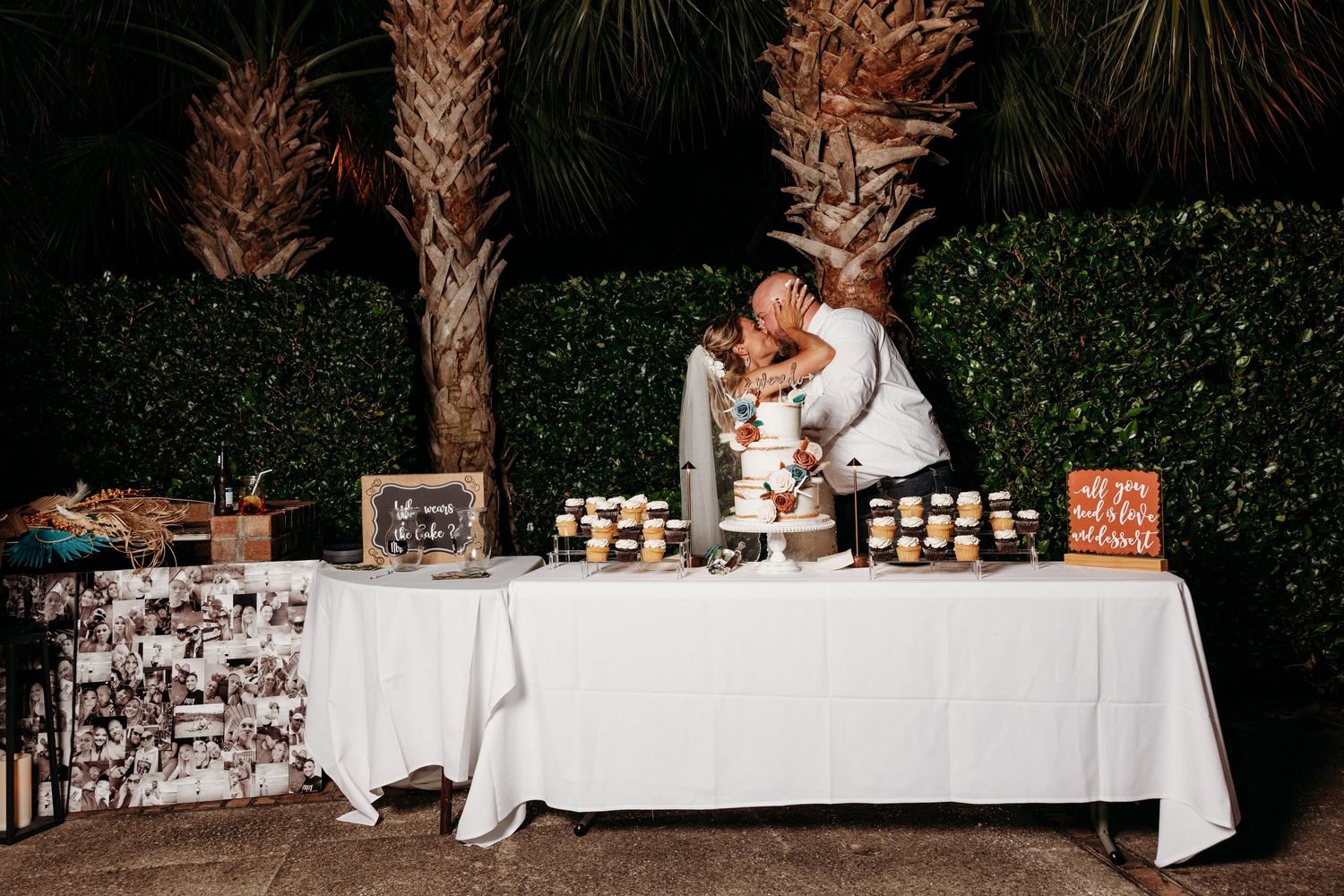 A long white reception table set up outdoors with palm trees in the background.