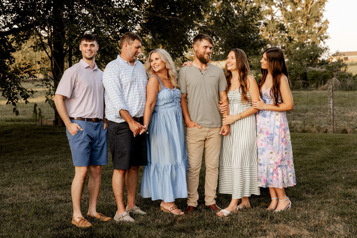 Family portrait at sunset with coordinated pastel outfits in an outdoor setting.
