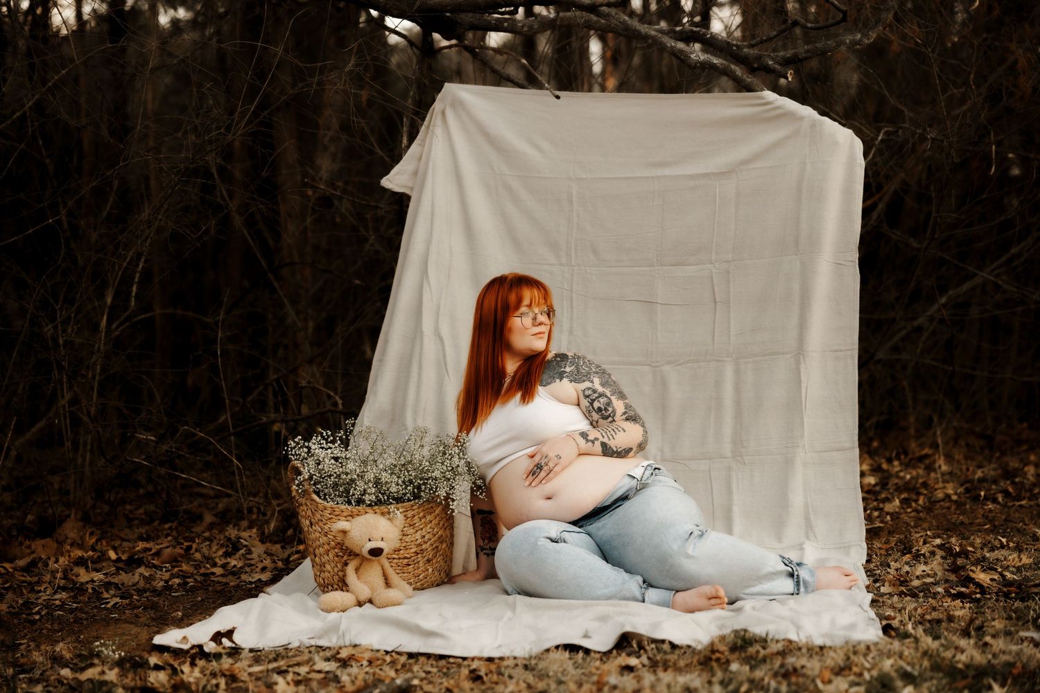 Artistic maternity portrait with white backdrop and teddy bear in outdoor setting.