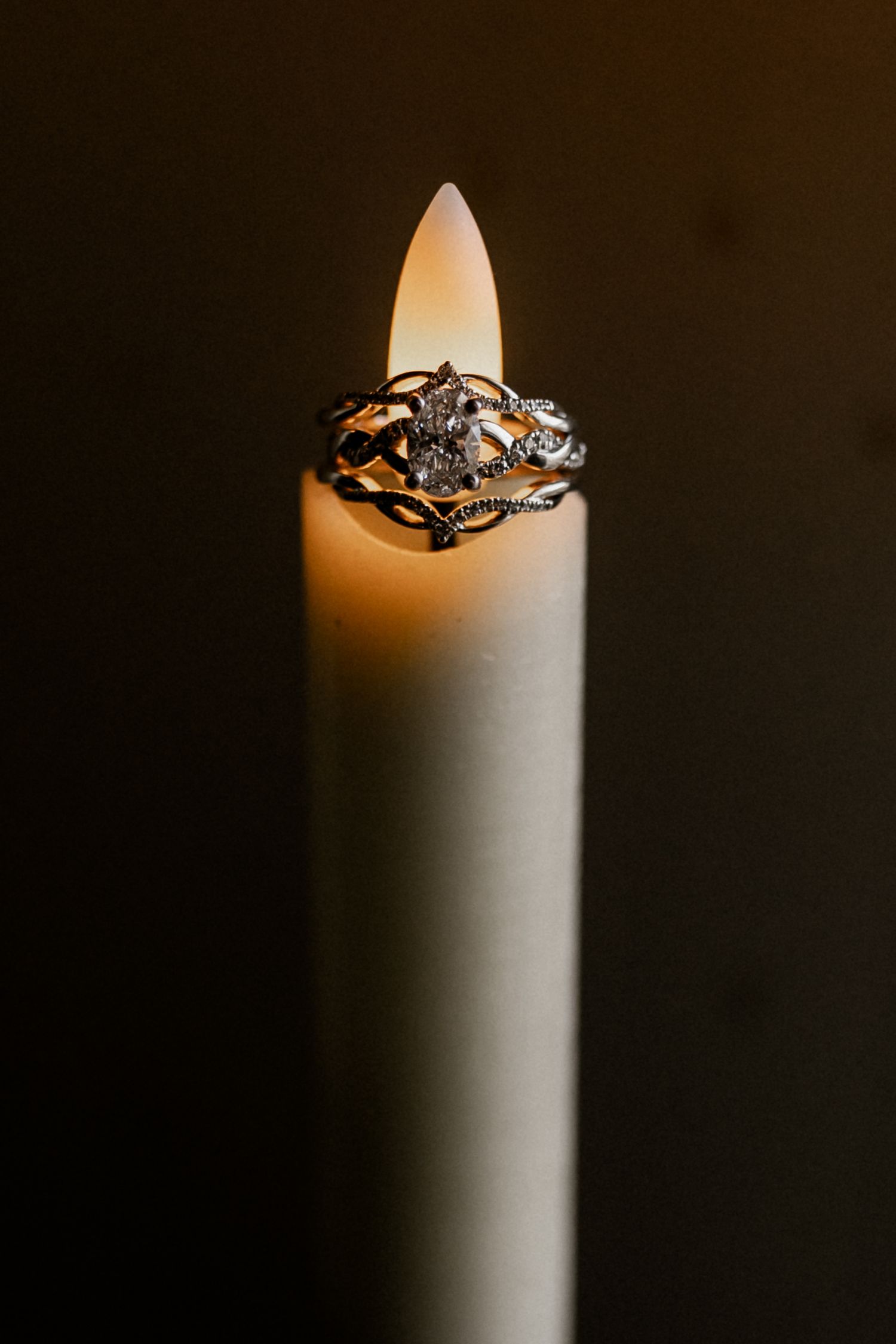 Close-up of a glowing white candle with rings balanced on top against dark background.