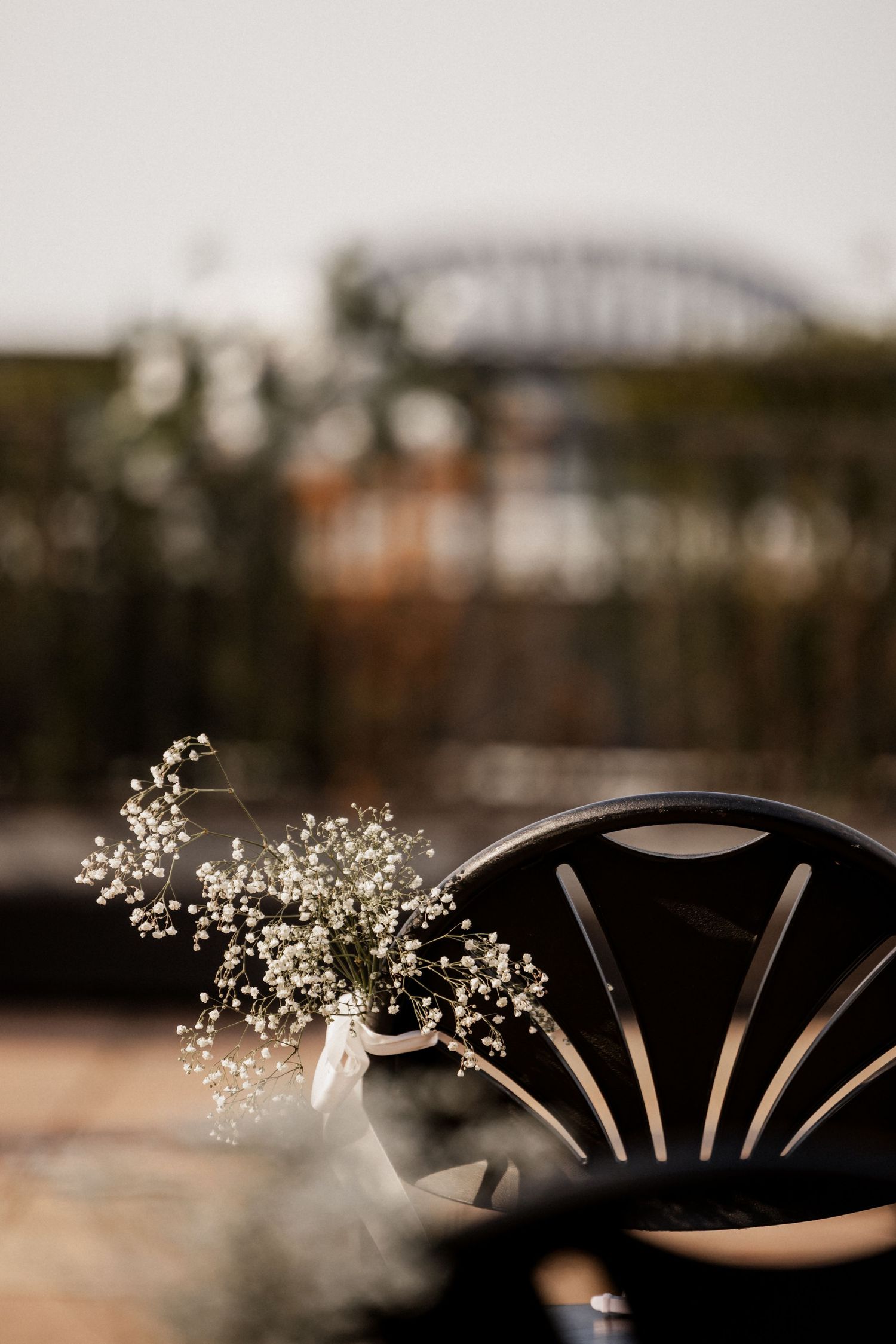 Baby's breath floral arrangement in black chair with blurred architectural background.