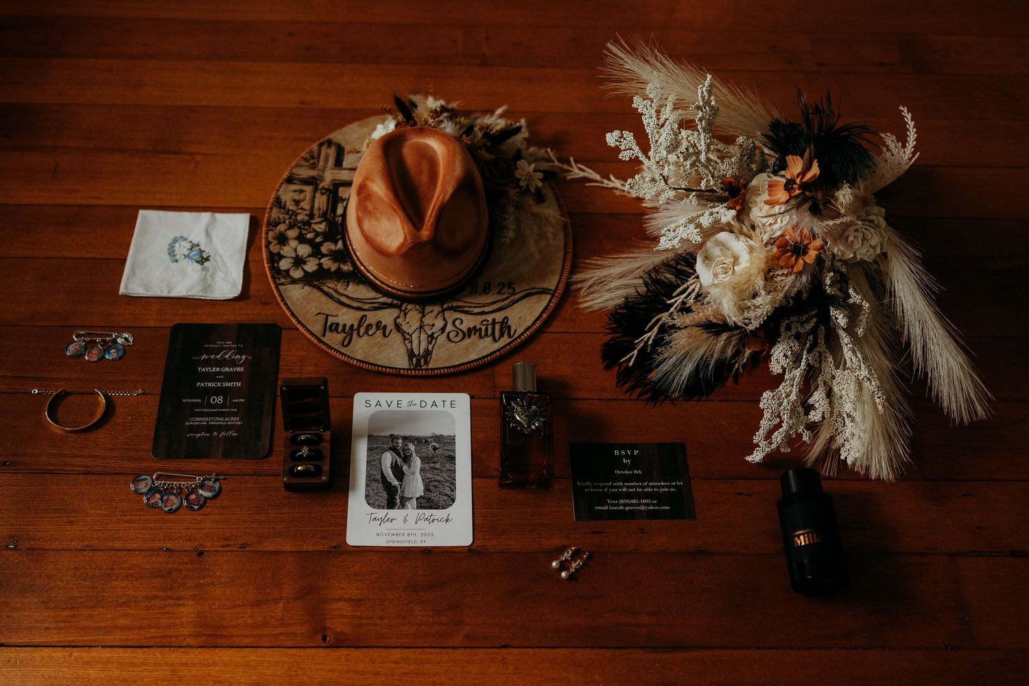 Rustic wedding flat lay with cowboy hat, floral bouquet, invitations, and accessories on wooden table.