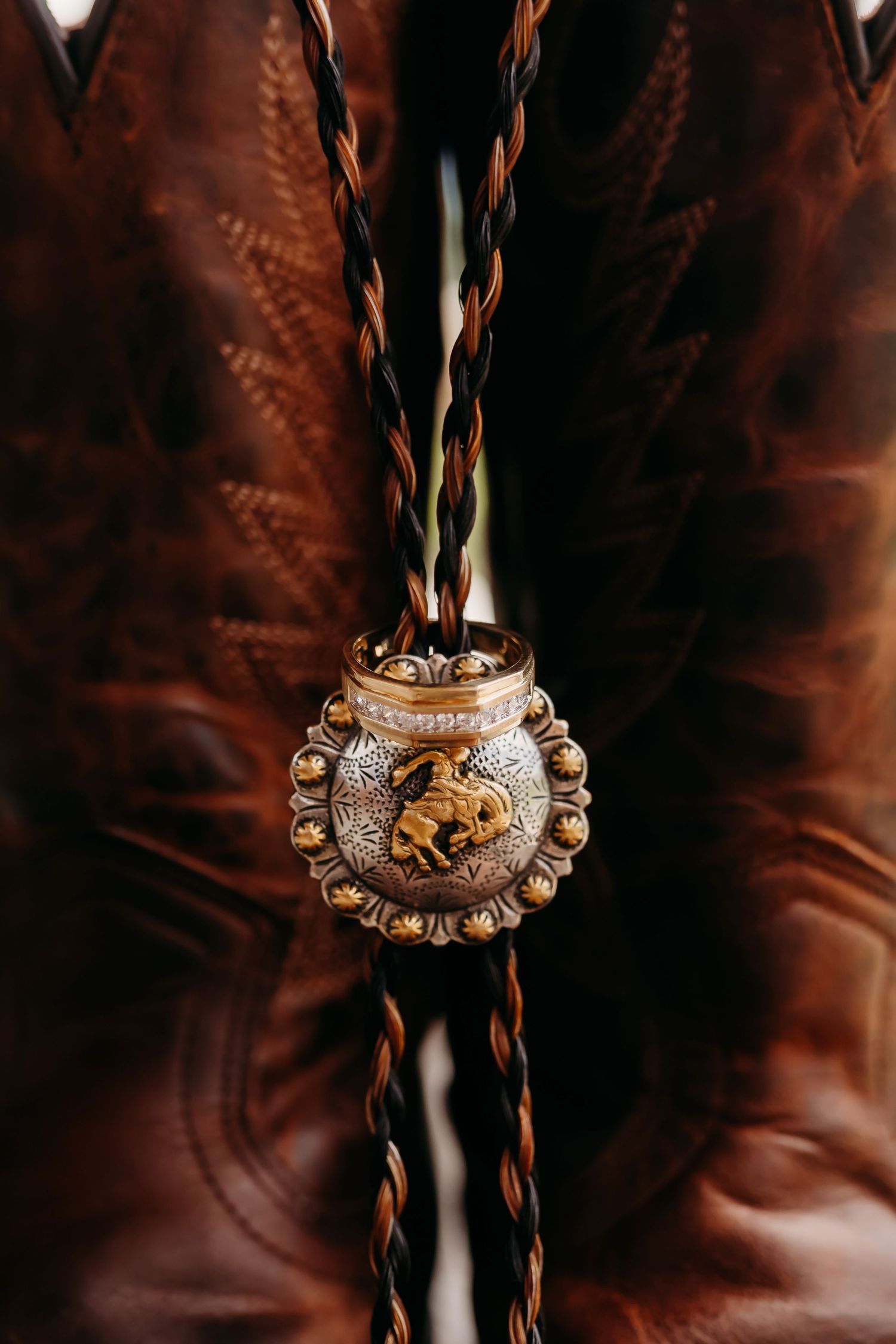 Western wedding bolo tie with ornate horse medallion displayed on brown leather cowboy boots.