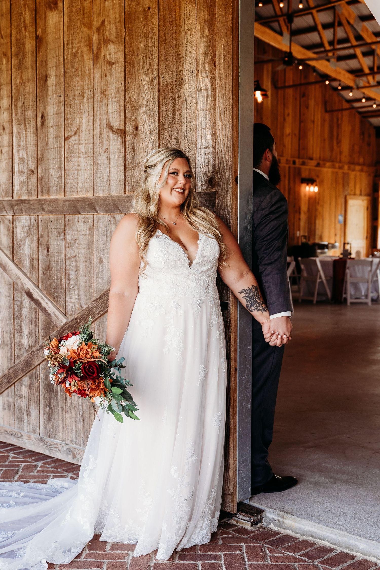 A wedding dress and bouquet photographed in a rustic barn venue with wooden walls and string lights.