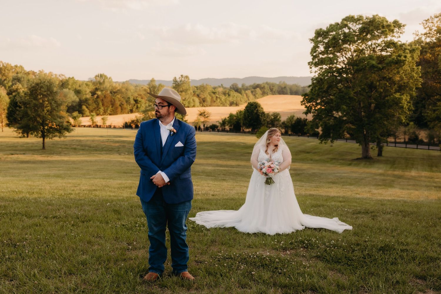 Bride and groom first look moment in golden hour light on scenic green countryside field.