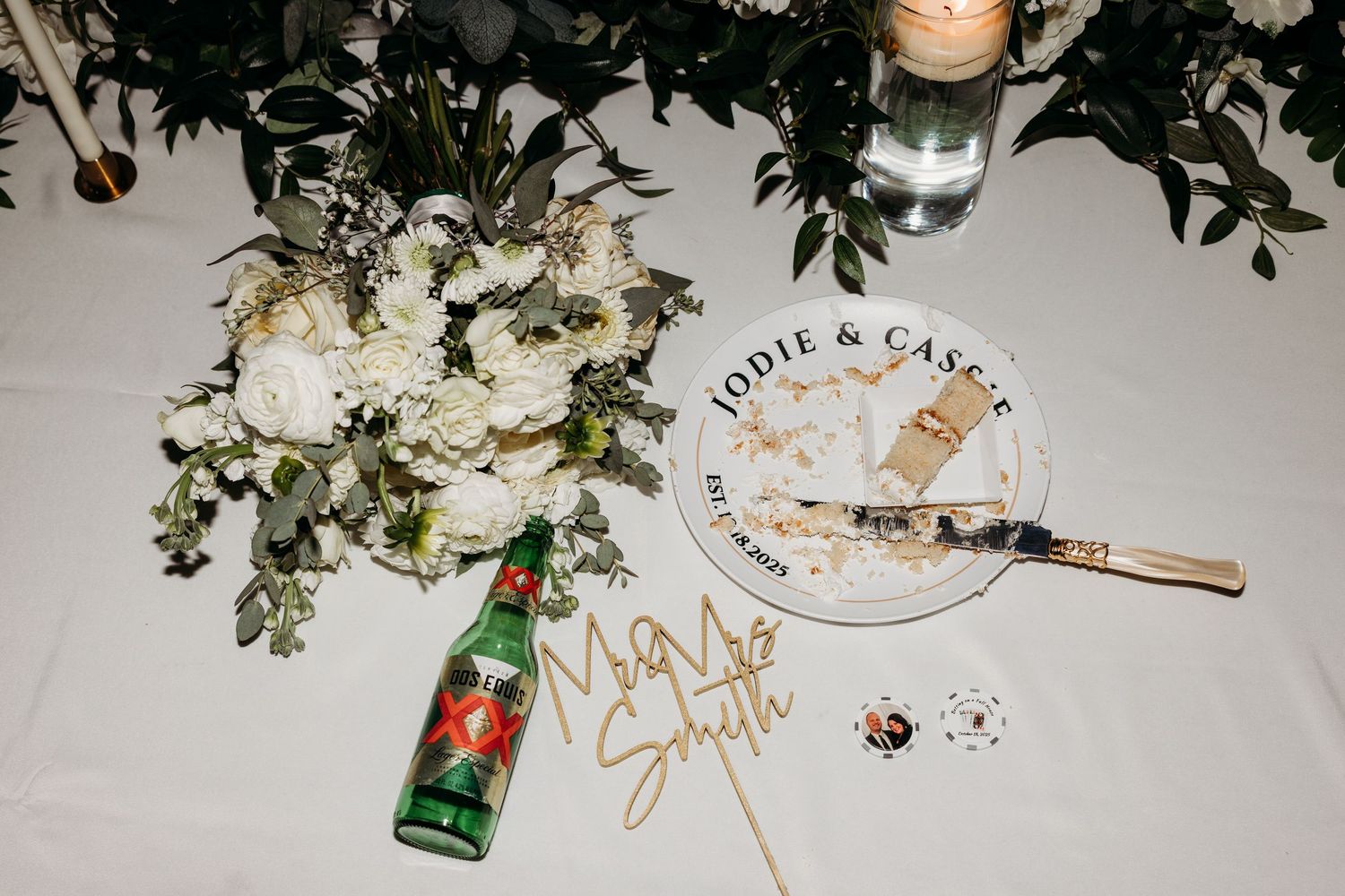 Wedding reception table with white floral bouquet, cake plate reading Jodie and Cassie, and decorative name sign.