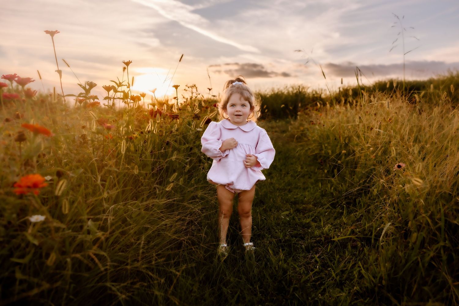 Small child stands in a field of wildflowers during golden hour wearing white clothing.