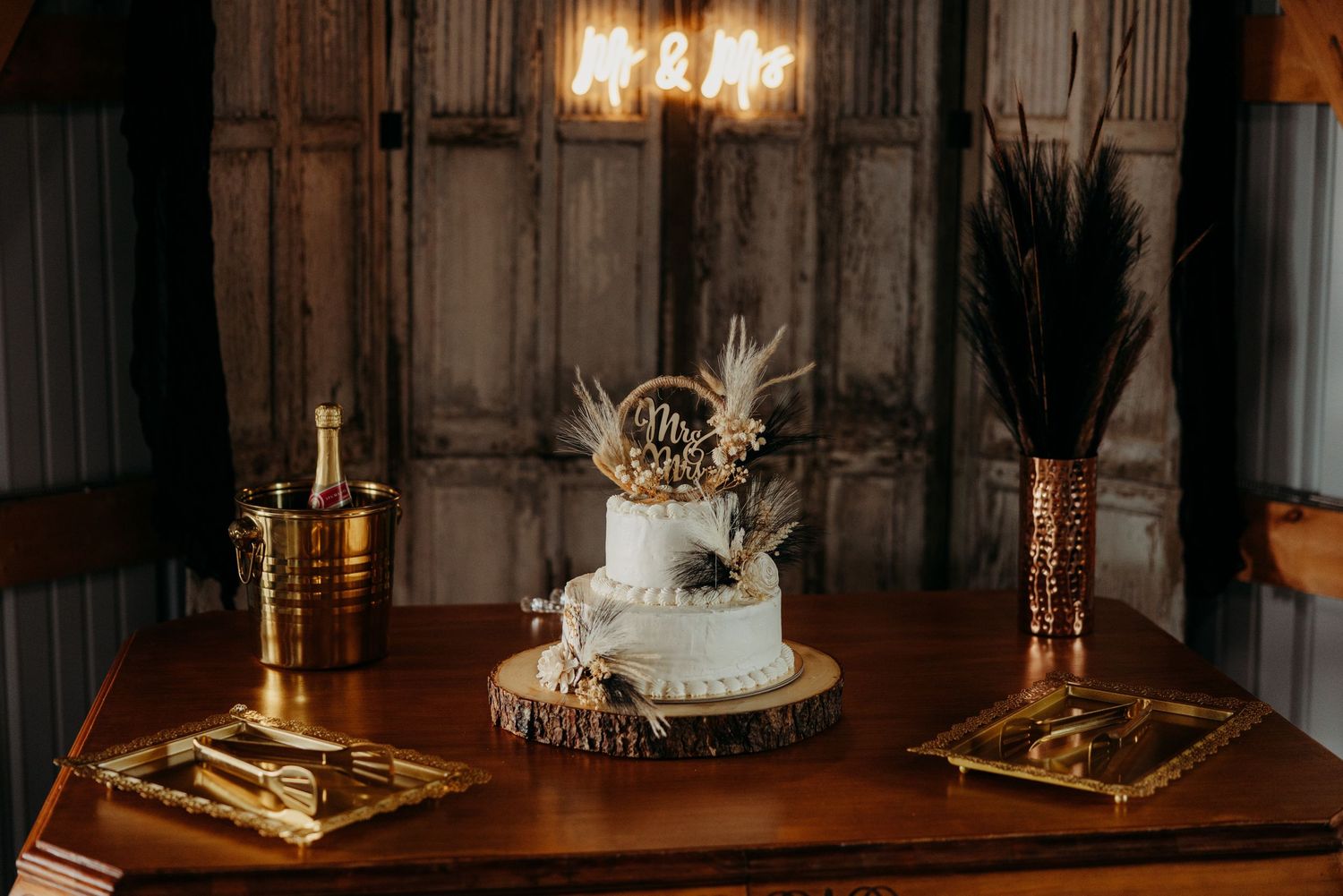 Elegant two-tier white wedding cake with dried floral topper displayed on rustic wooden table.