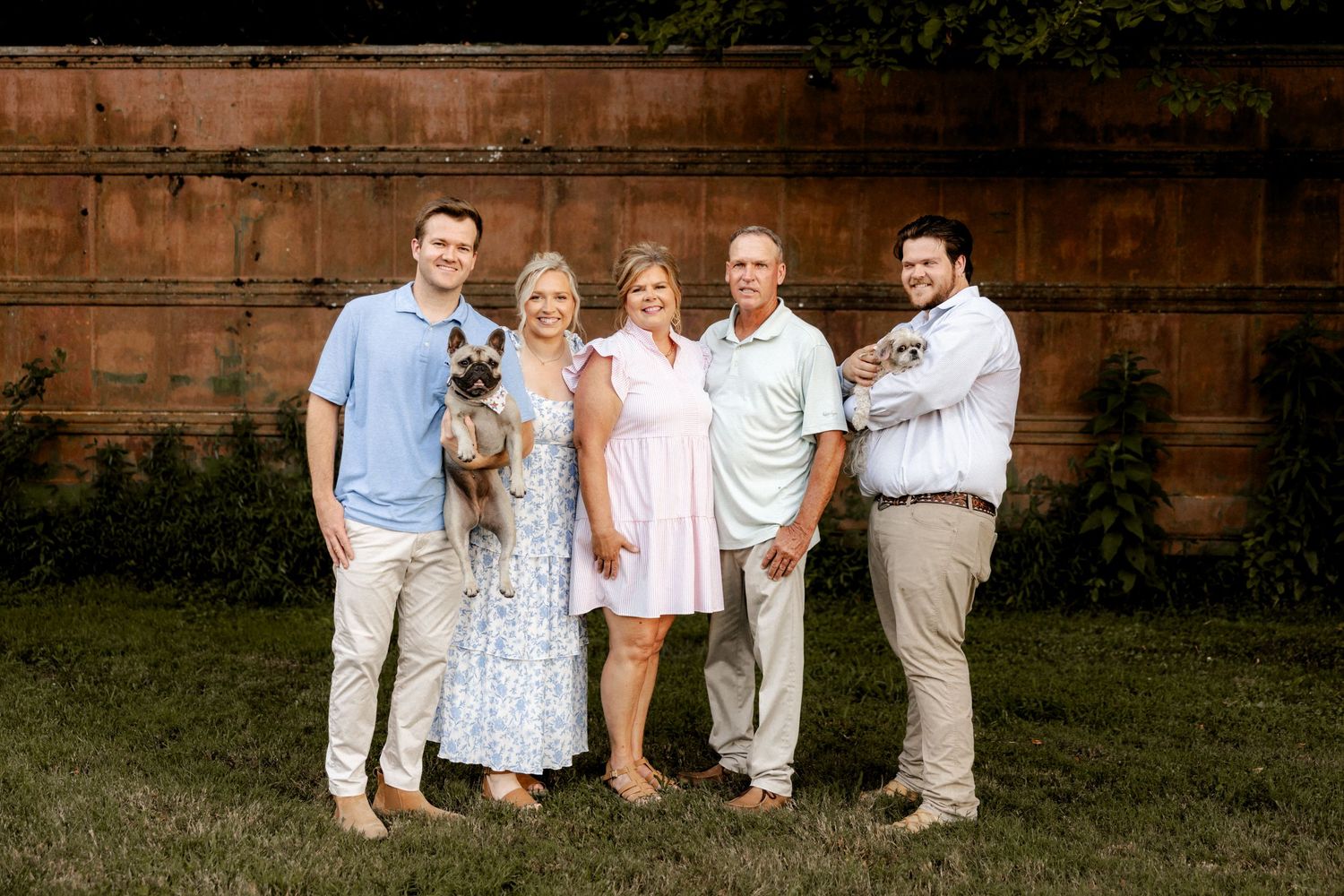 Extended family group posed casually against brick wall backdrop in coordinated summer attire.