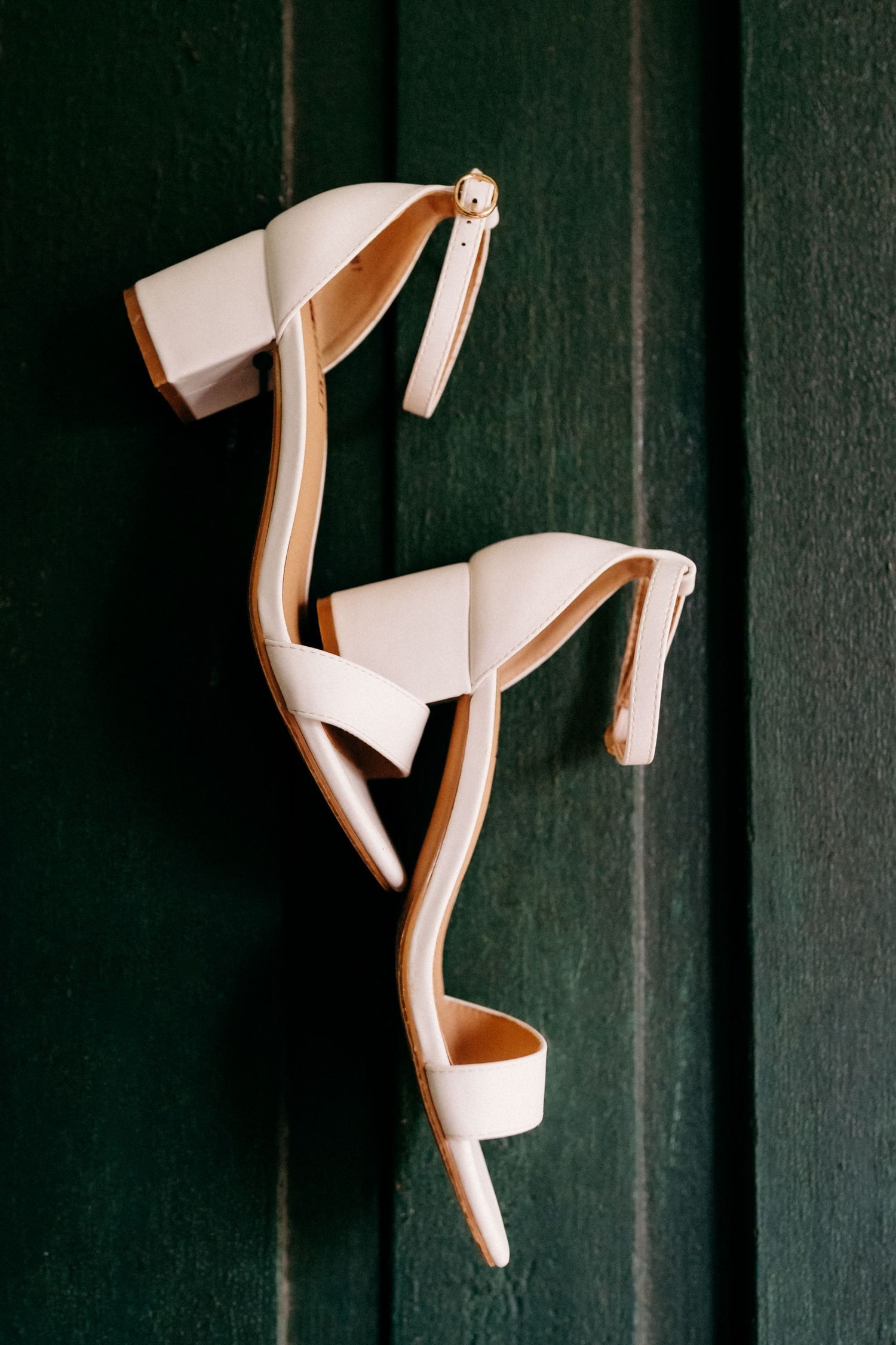 White block heel sandals with ankle strap displayed against a dark green wooden background.