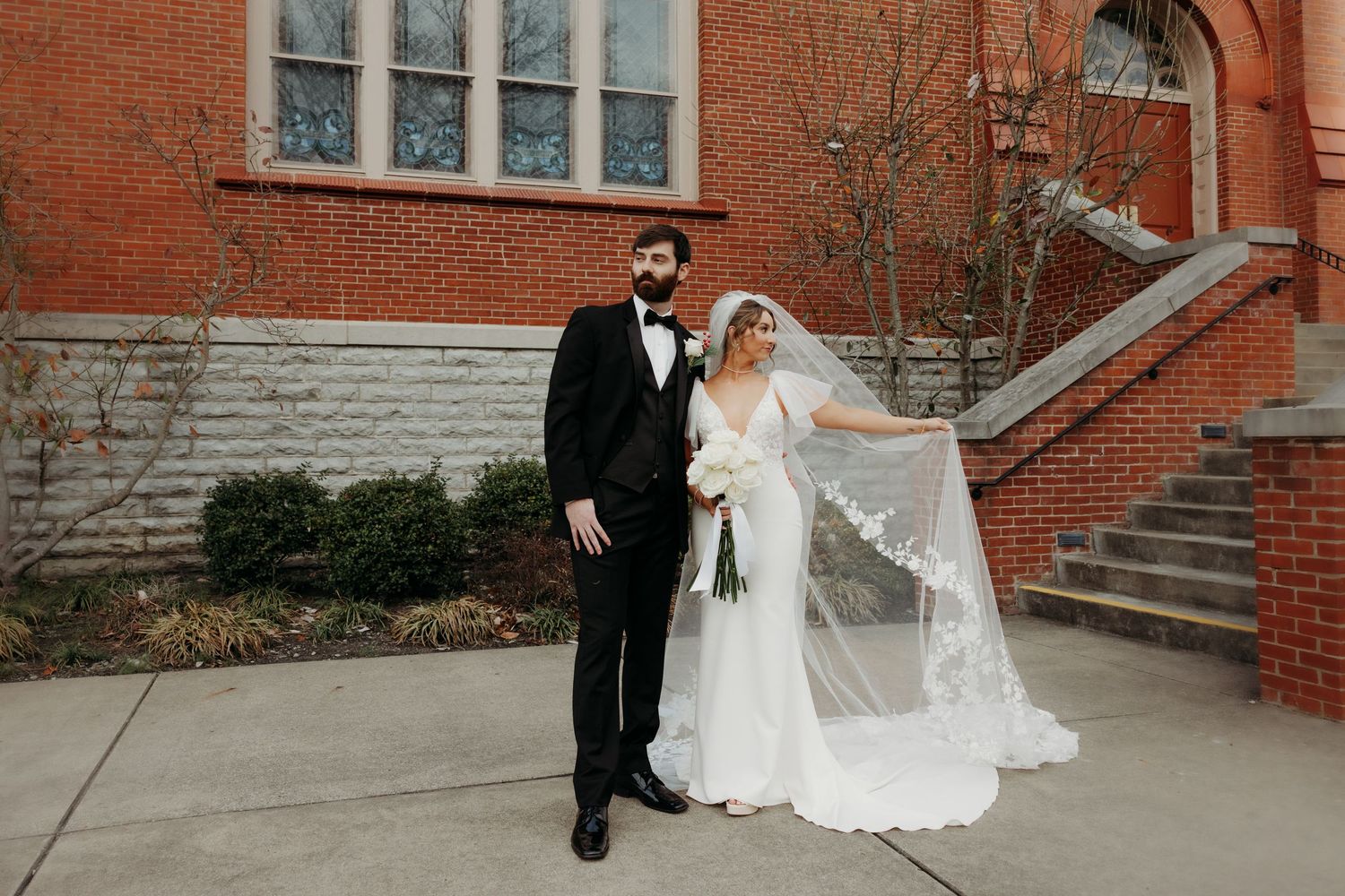 A classic wedding portrait in front of a red brick church with stone steps and flowing veil.