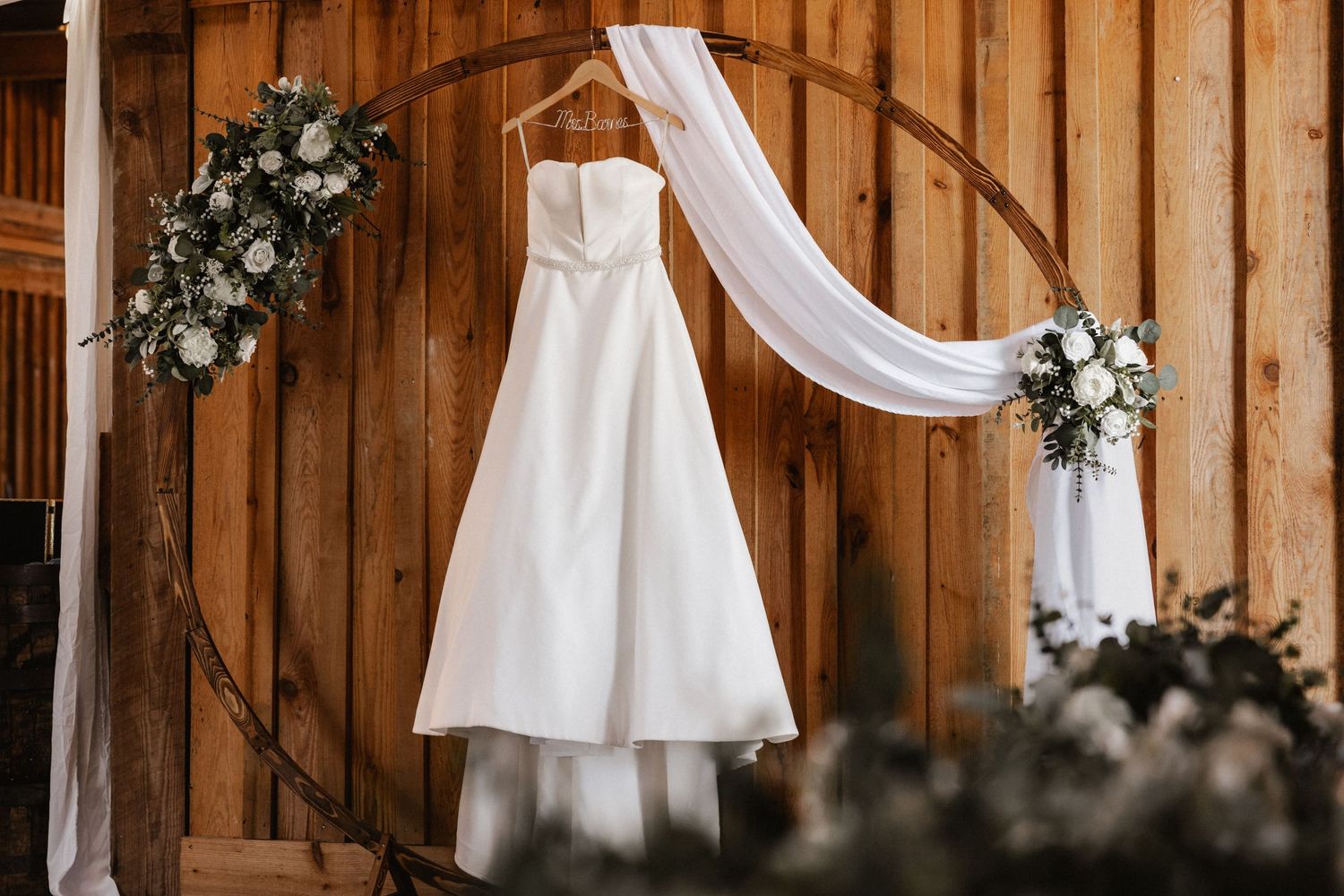 White fabric draping and floral arrangements decorating a rustic wooden barn interior at The Hilt.