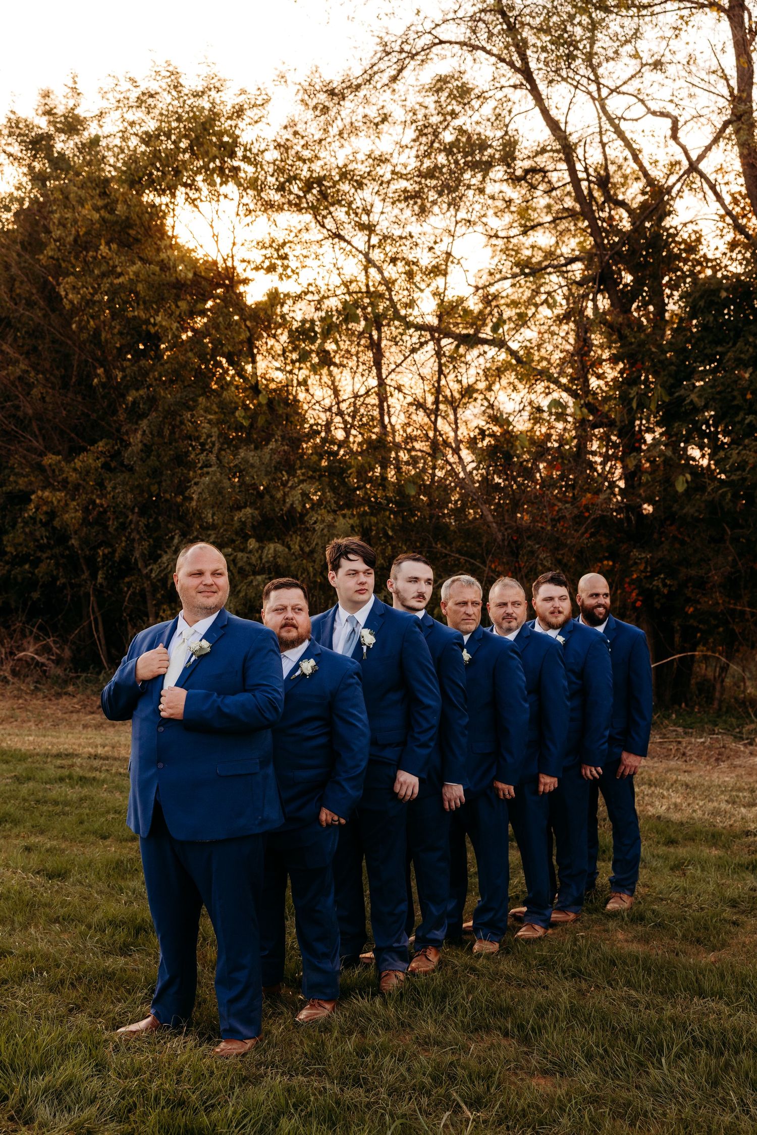 Groomsmen in navy suits pose in line formation at sunset.