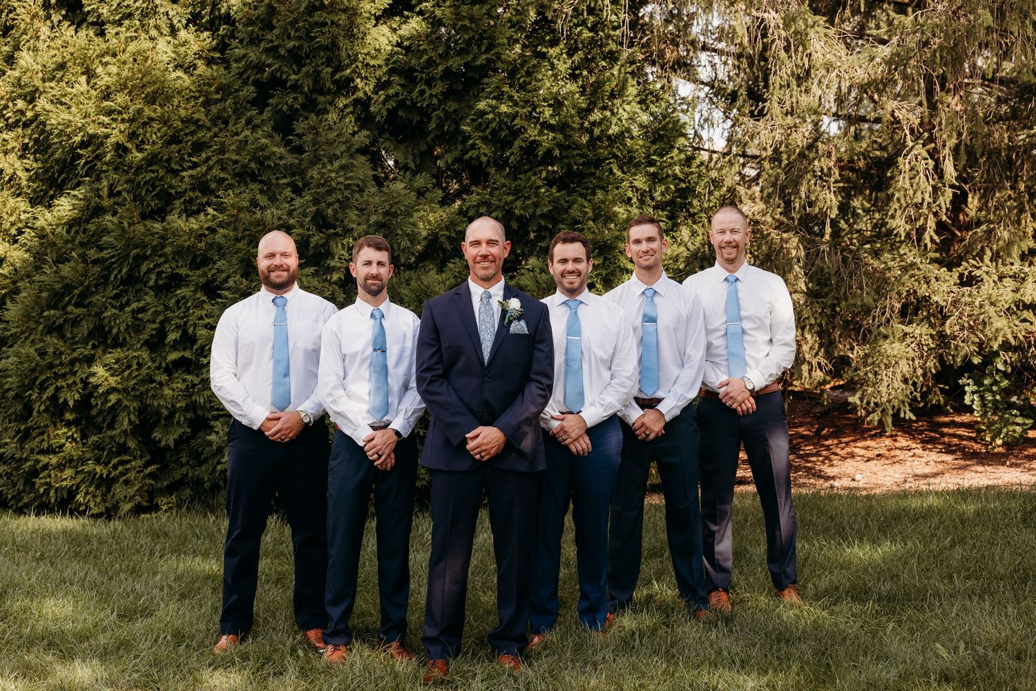Groomsmen in navy suits posing for formal wedding photos on grass.