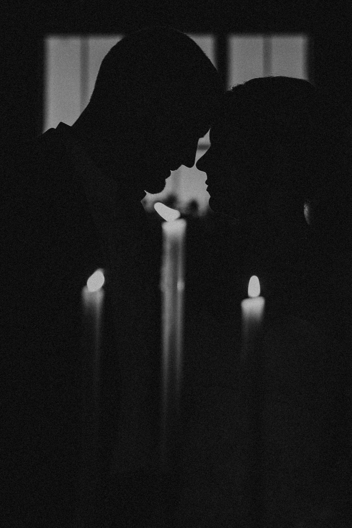 Silhouetted bride and groom in a dark space with glowing candles creating an editorial dramatic atmosphere.
