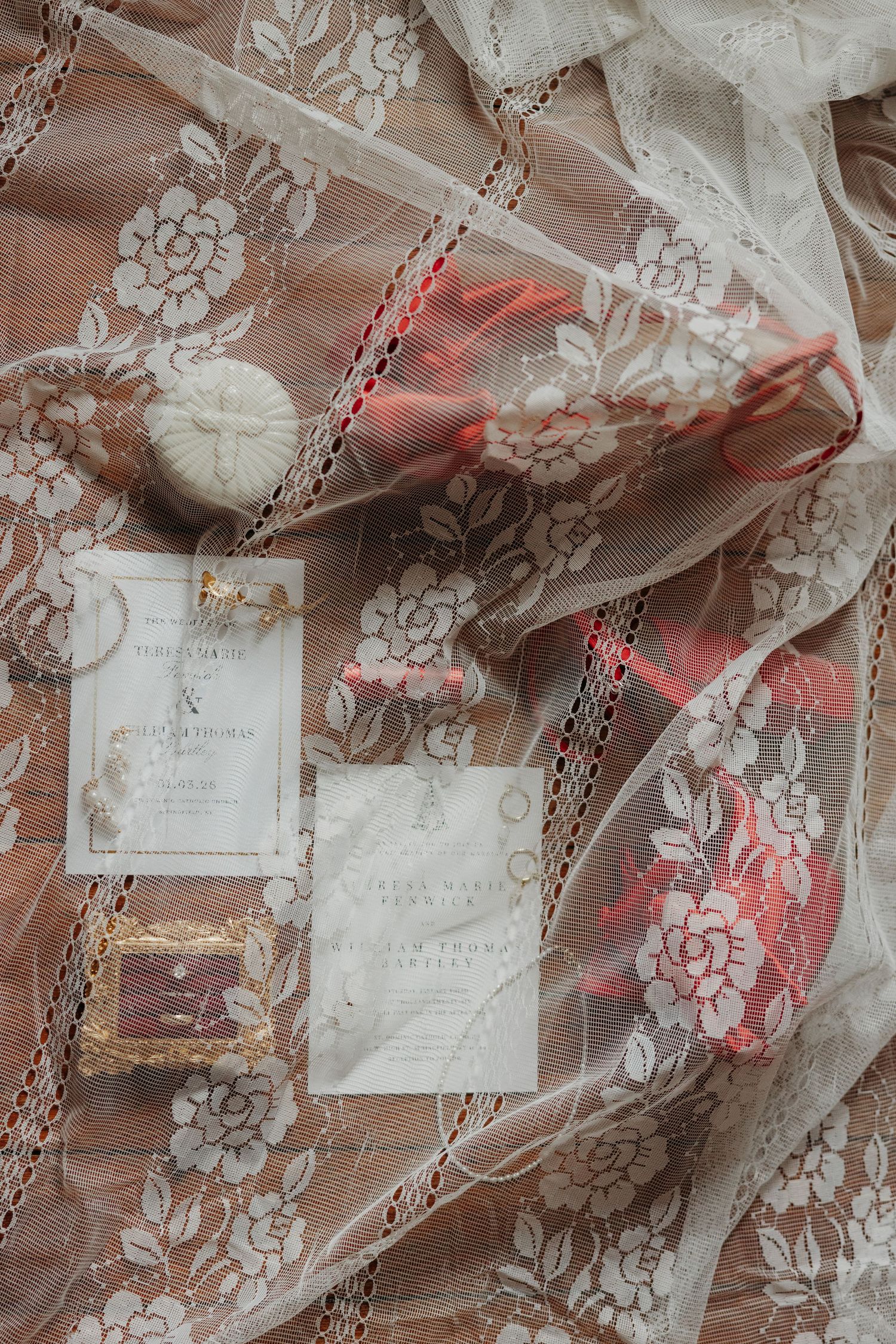 Elegant wedding flat lay with lace fabric, invitation suite, ring box, and coral floral accents.