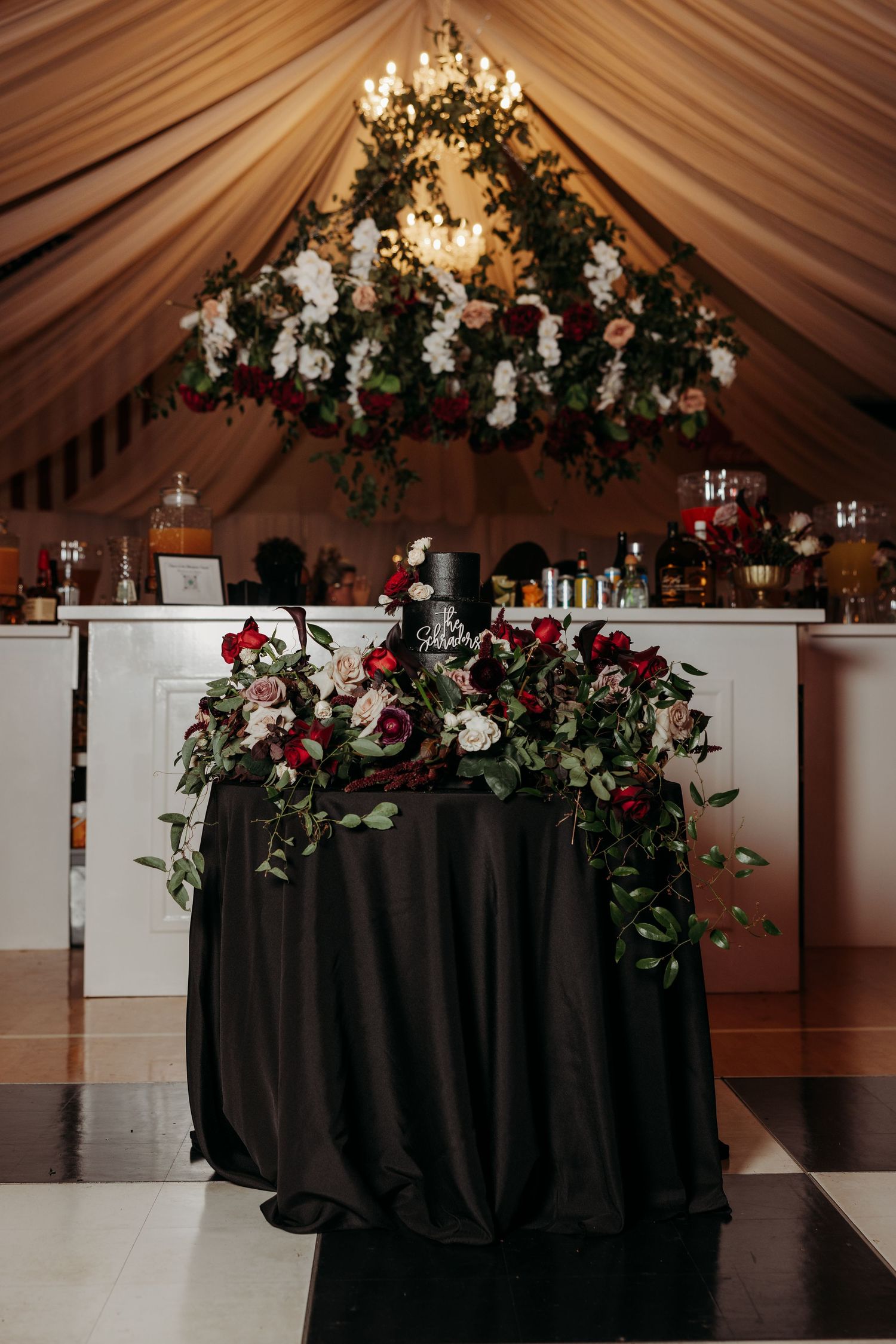Romantic sweetheart table with black linen, red and white roses, and floral chandelier above bar.