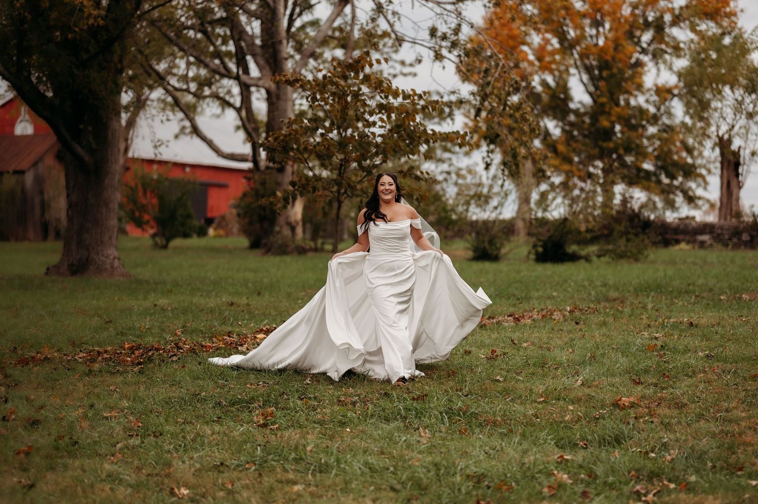 Bride celebrates wedding day on grassy field with autumn trees in background.