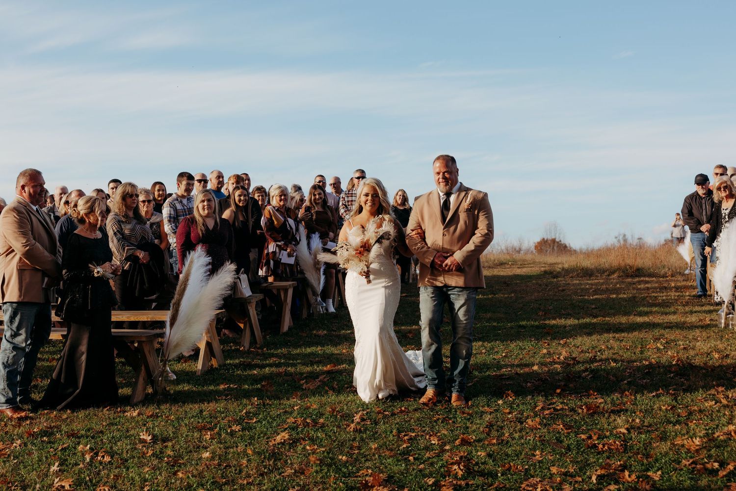 Bride and groom walk back down aisle after outdoor fall wedding ceremony with guests applauding.
