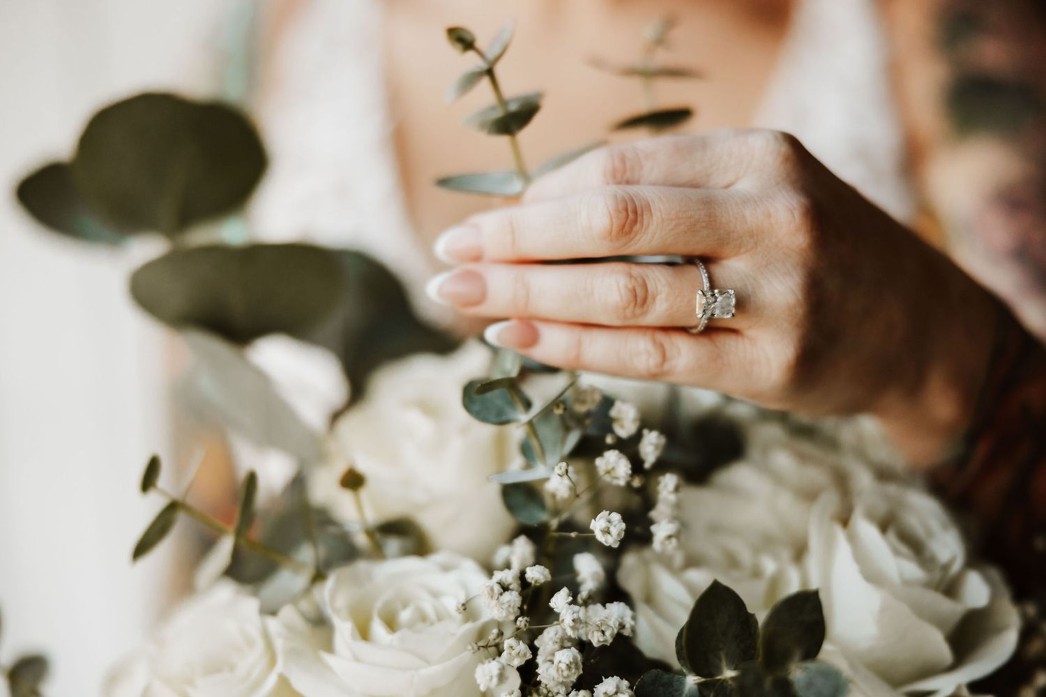 Close-up of white roses and eucalyptus in a bridal bouquet with engagement ring detail at Silo Farms wedding venue.