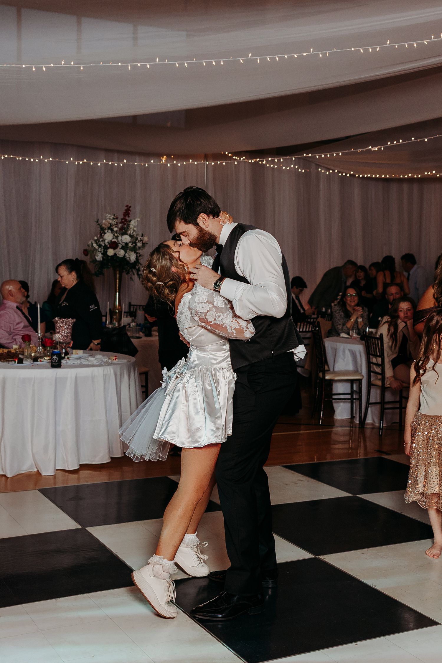 Couple dancing at wedding reception under string lights on checkered dance floor.