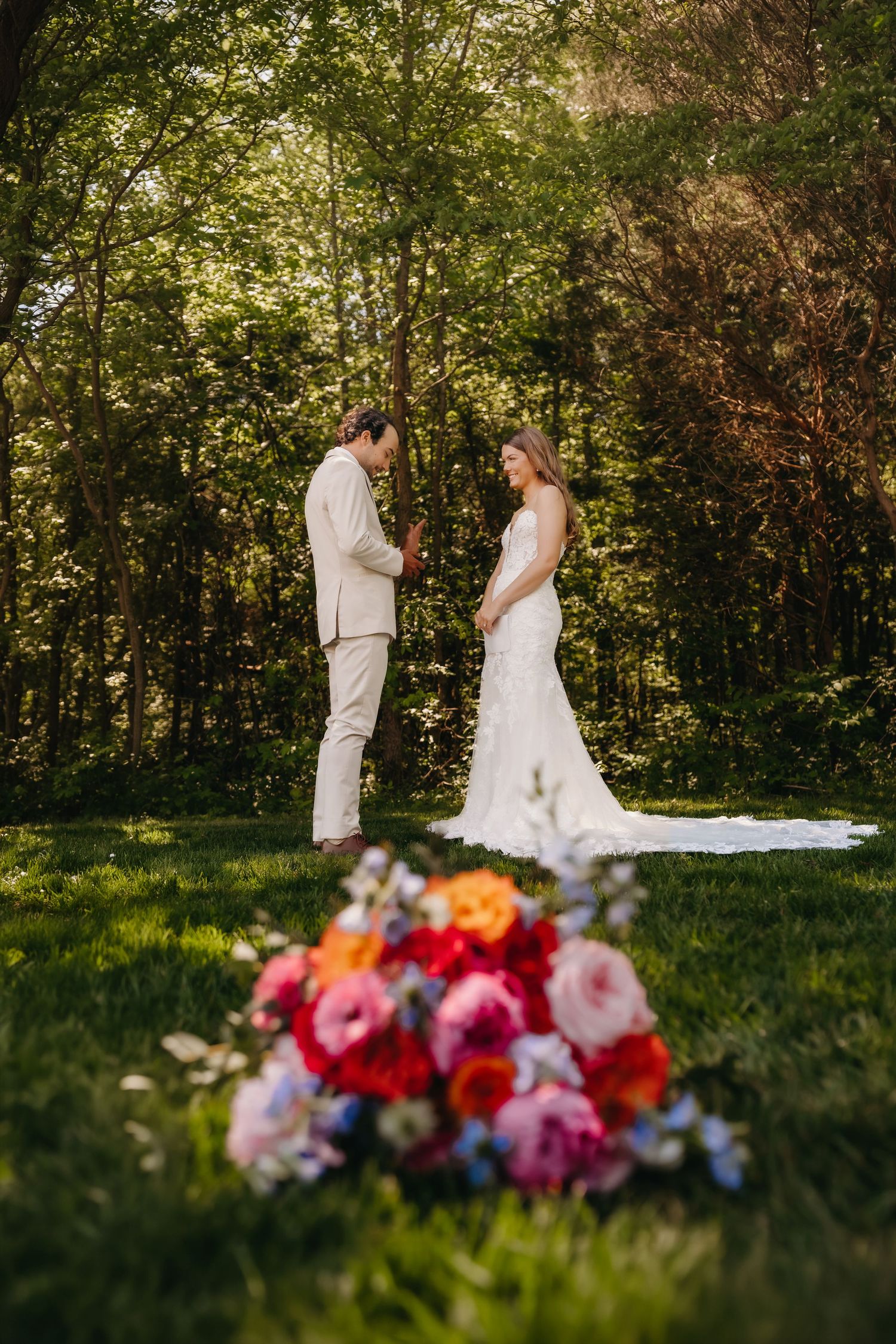 Bride and groom hold hands in a sunlit garden with colorful floral bouquet in the foreground.