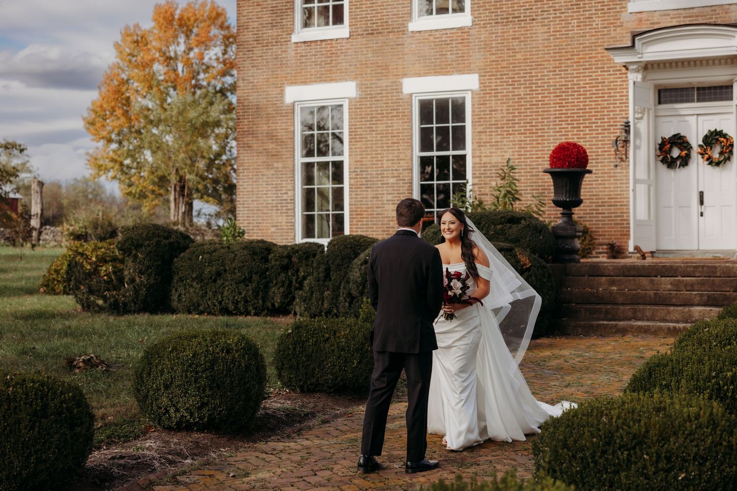 Bride and Groom first look outside a brick mansion with fall foliage and decorative wreaths.