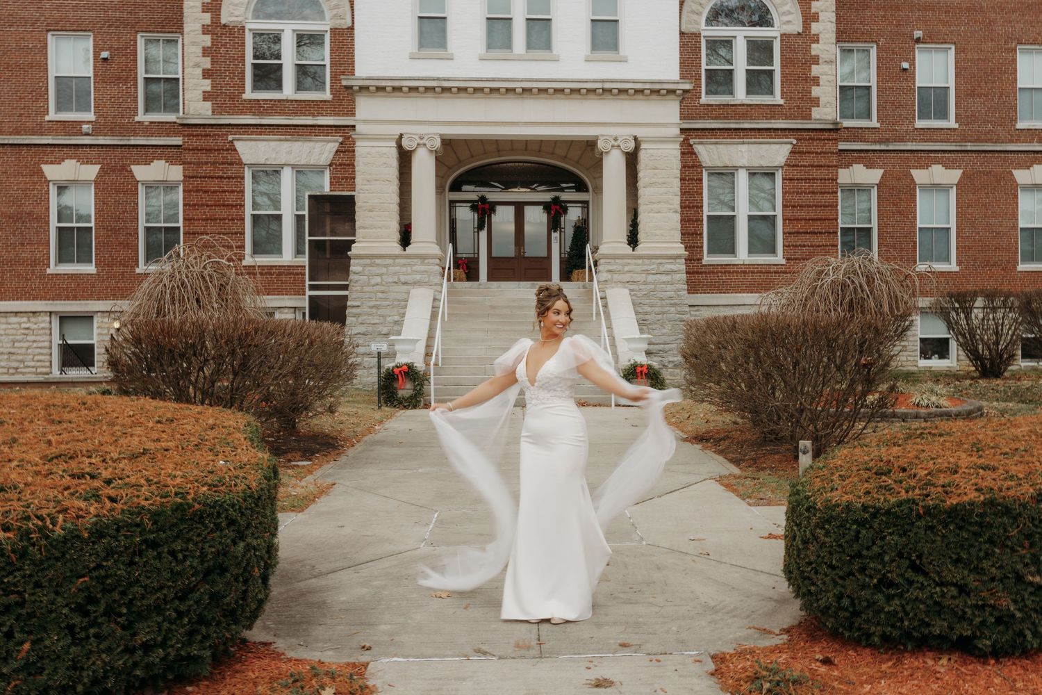 Bride twirling in white dress on stone steps of brick building with fall leaves.