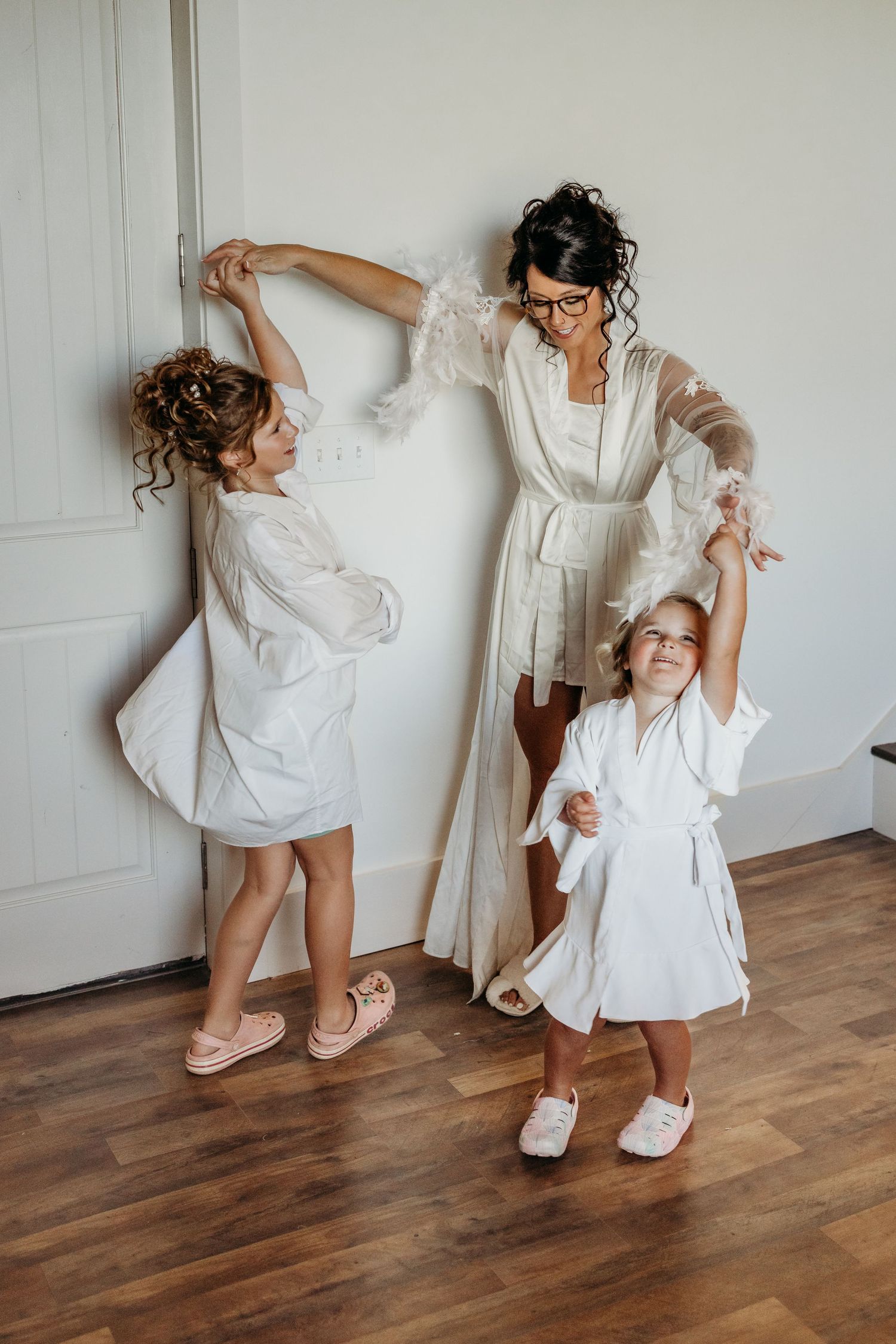 Playful wedding preparation photos with white dresses and pink slippers on hardwood floor.