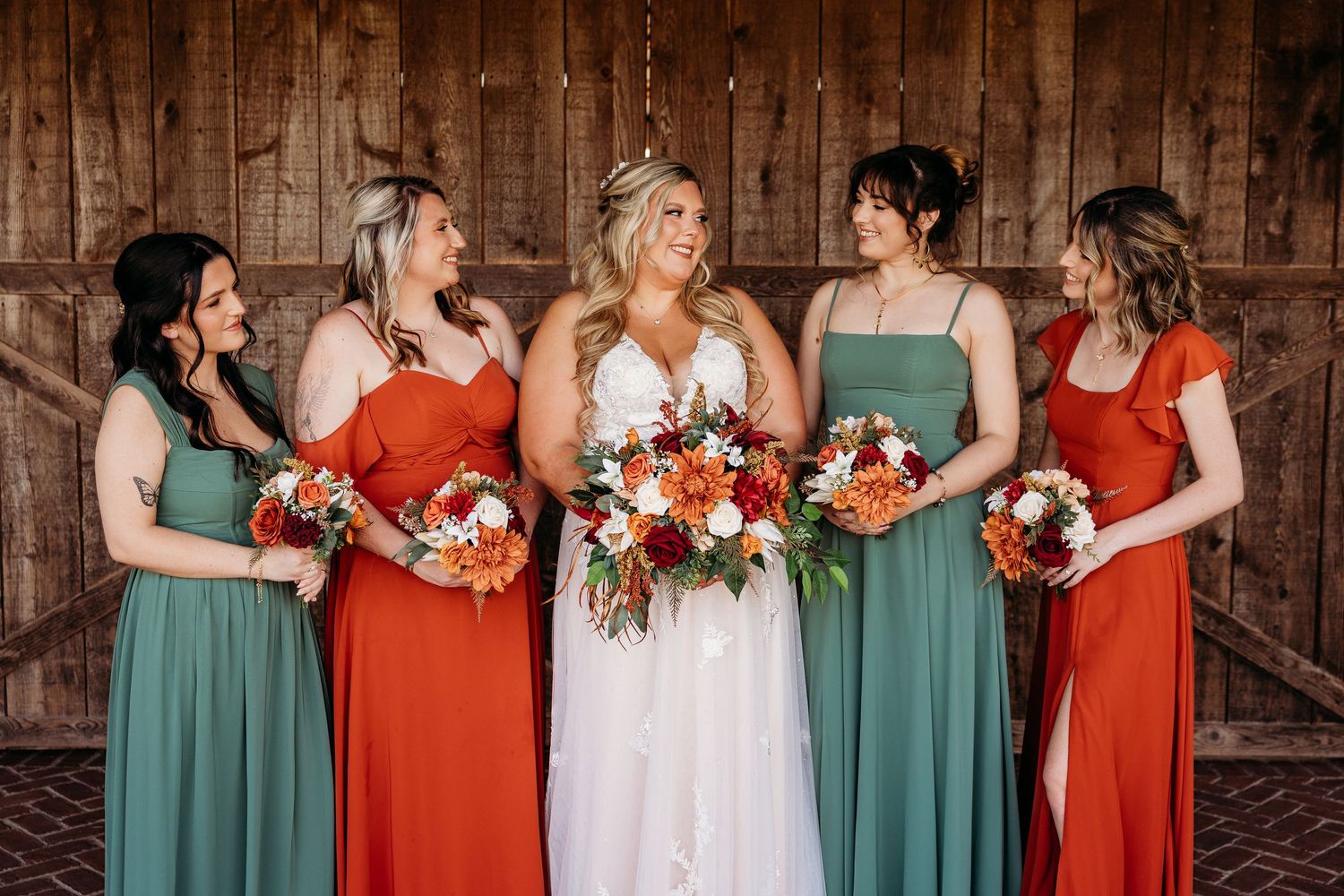 Bridesmaids in alternating teal and red dresses pose with bouquets at a rustic venue in Finchville, KY.