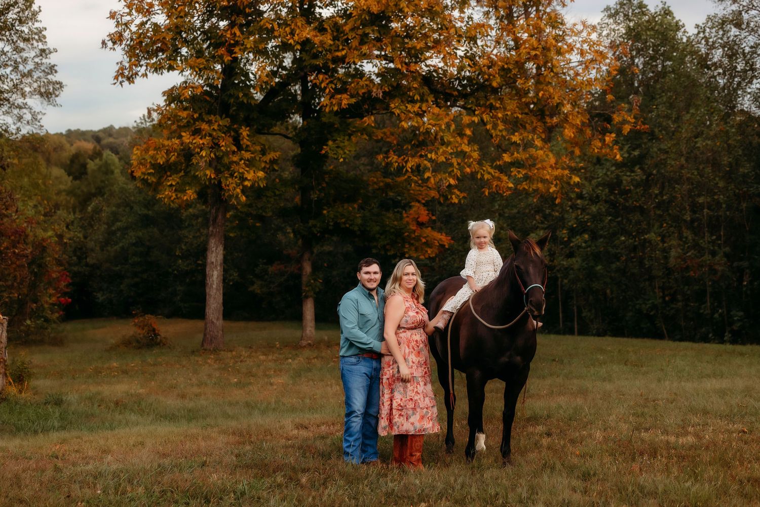 A beautiful autumn photoshoot in a field at sunset with a horse and people against golden trees.